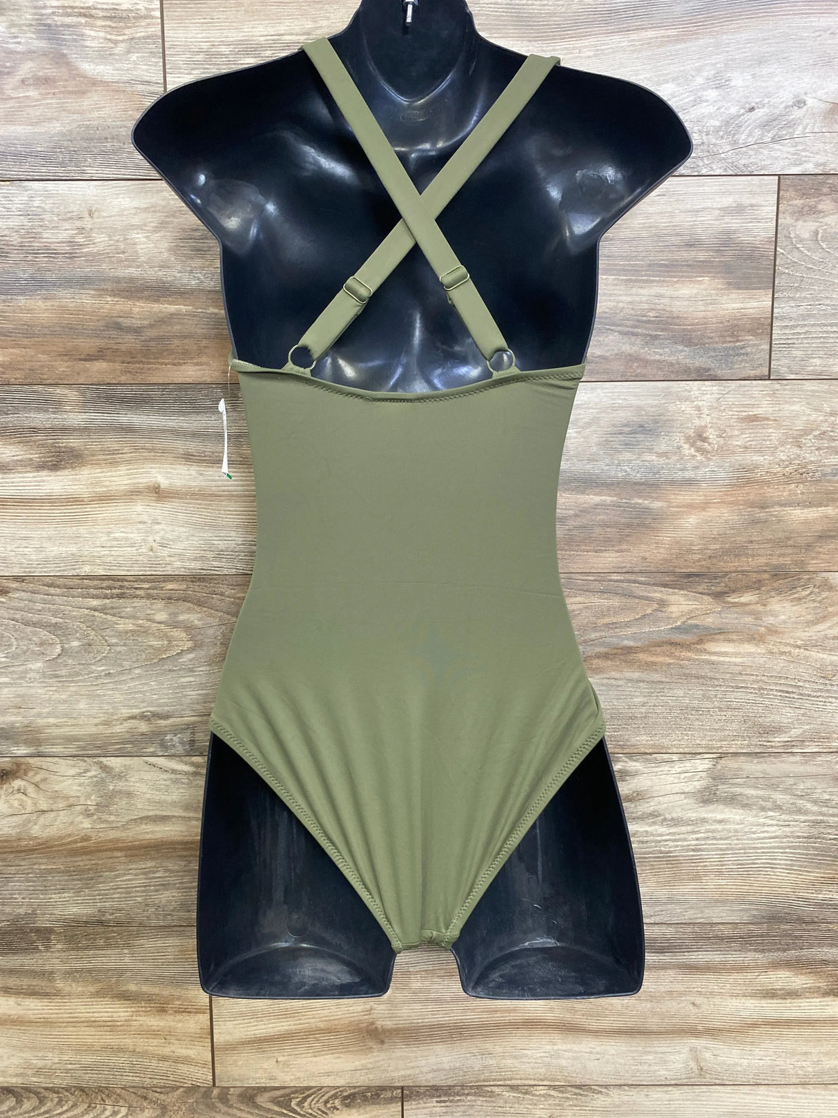 Back view of green maternity one-piece swimsuit showing crossed adjustable straps and smooth full-coverage torso on black mannequin against wood floor