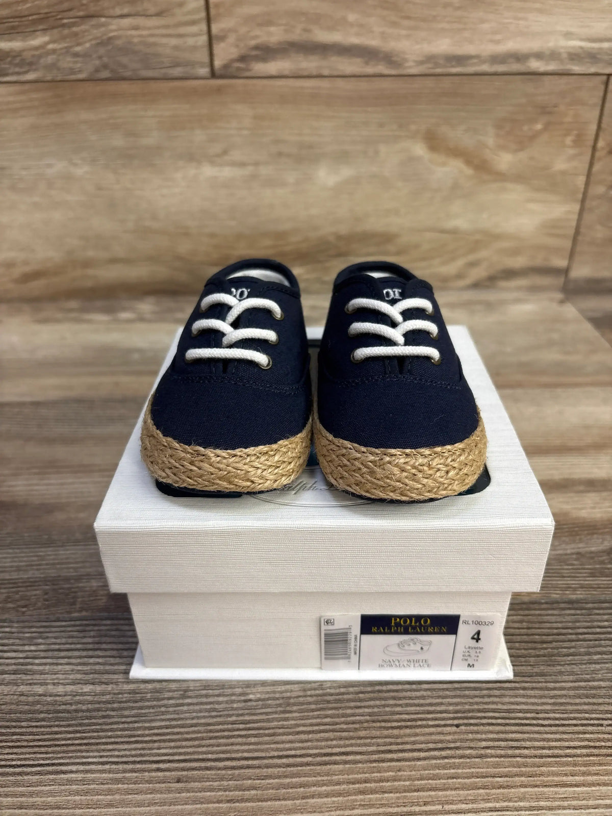 Front view of navy Ralph Lauren Bowman lace crib shoes showcasing white laces and braided rope soles on a shoebox