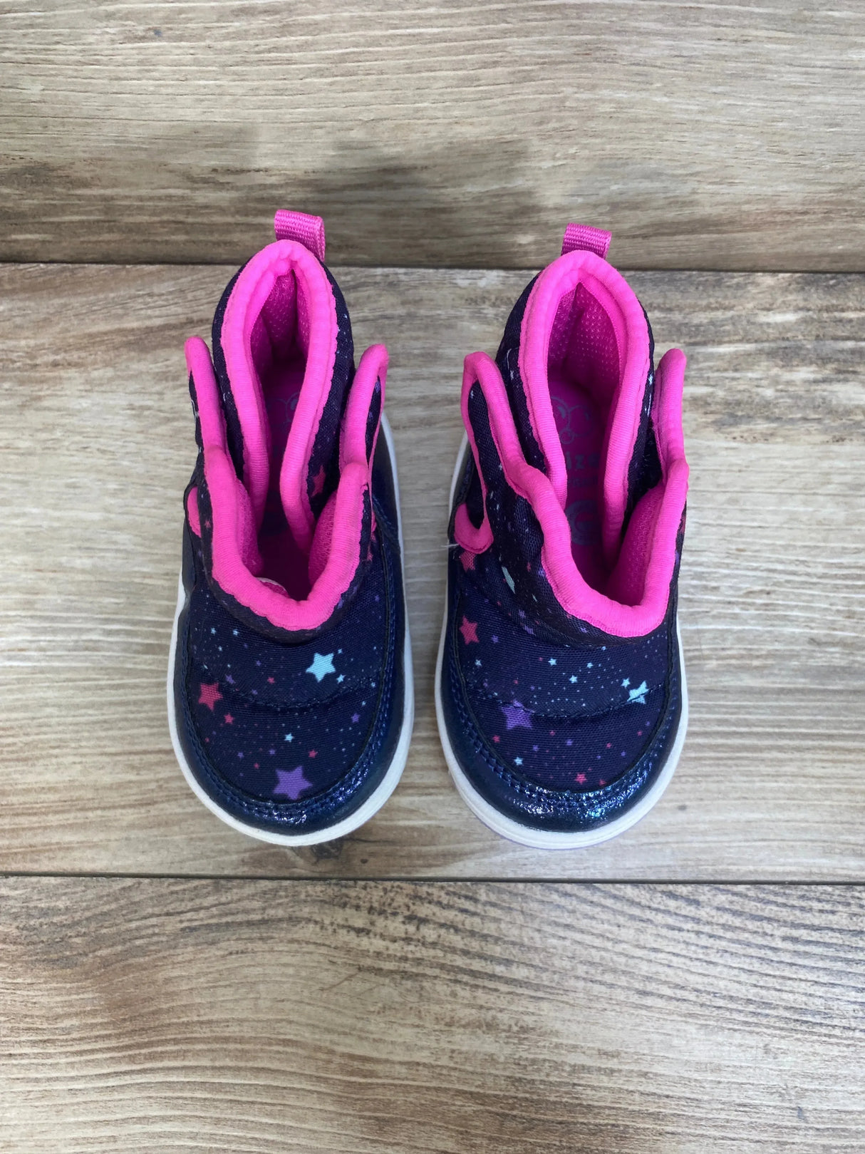 Top view of Surprize by Stride Rite Aster boots showing navy star print, bright pink lining and white soles on wood background