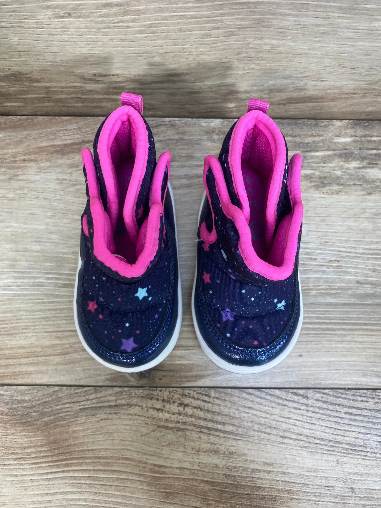 Top view of Surprize Stride Rite Aster boots showcasing navy with star print and pink fleece collar on wood plank floor