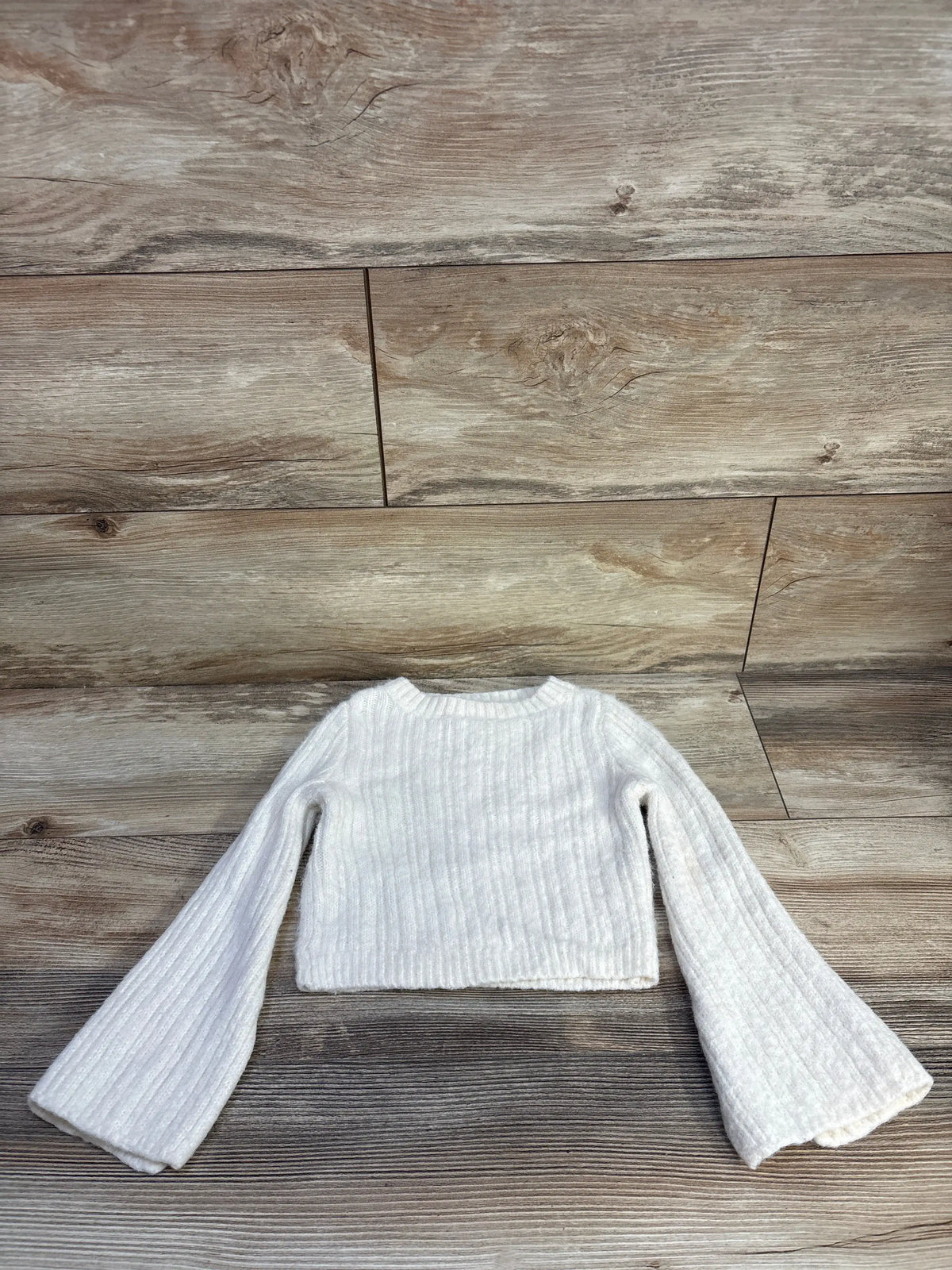 Front view of GB Girls ivory knit sweater in size 5T showcasing ribbed texture and flared sleeves on a wood-look background