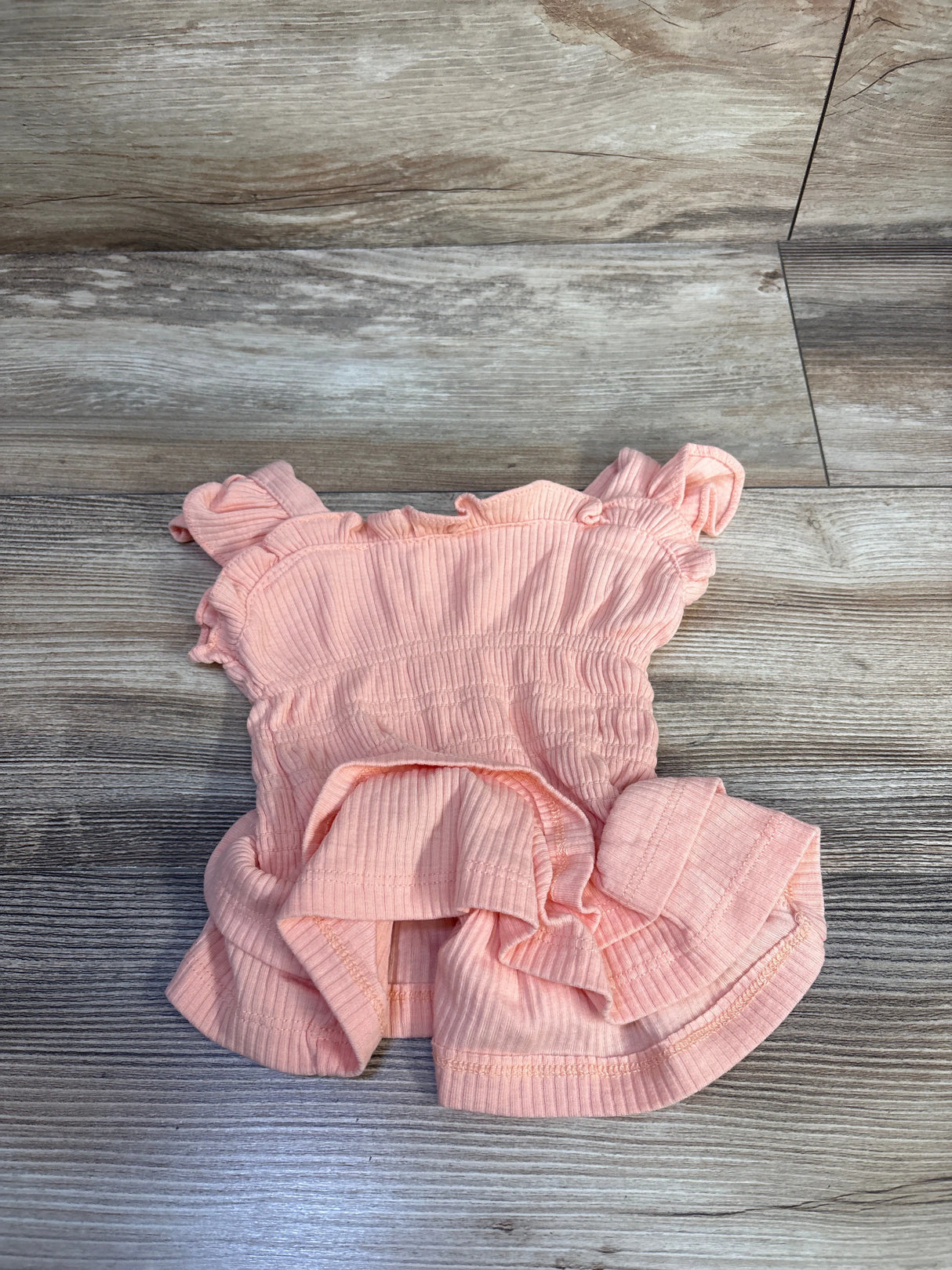 Flat lay of peach toddler smocked tank top showing ruffle straps and ribbed texture on wood floor