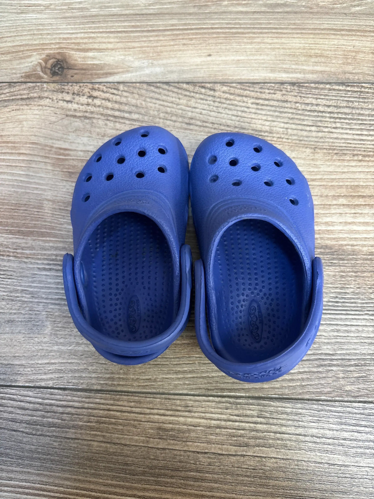 Top down view of Crocs Classic Clog toddler size 4/5 in blue showing ventilation holes and heel strap on wood floor