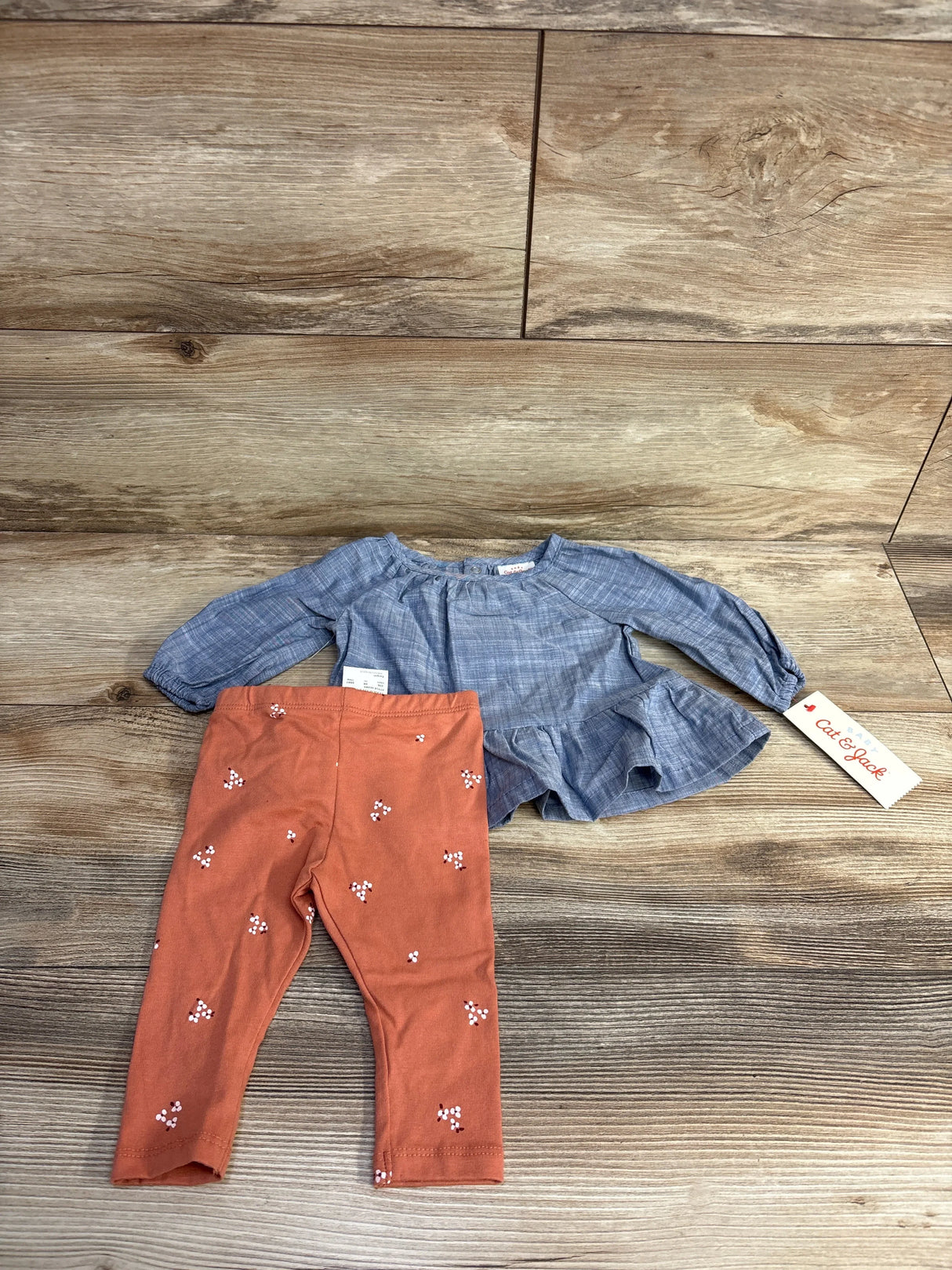 Baby girl outfit with blue long sleeve top and orange floral leggings on wood background