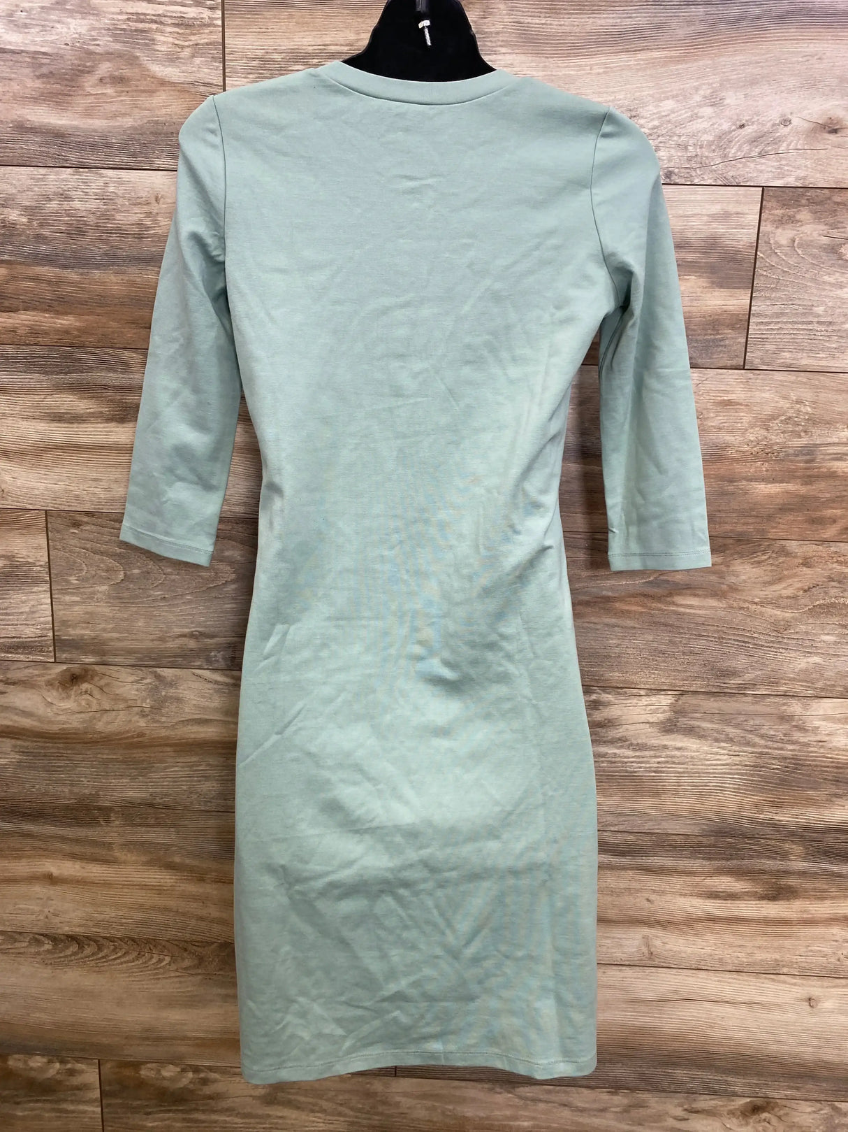 Back view of Lou Lou faux henley maternity dress in sage green showing three quarter sleeves and knee length fit on wood backdrop