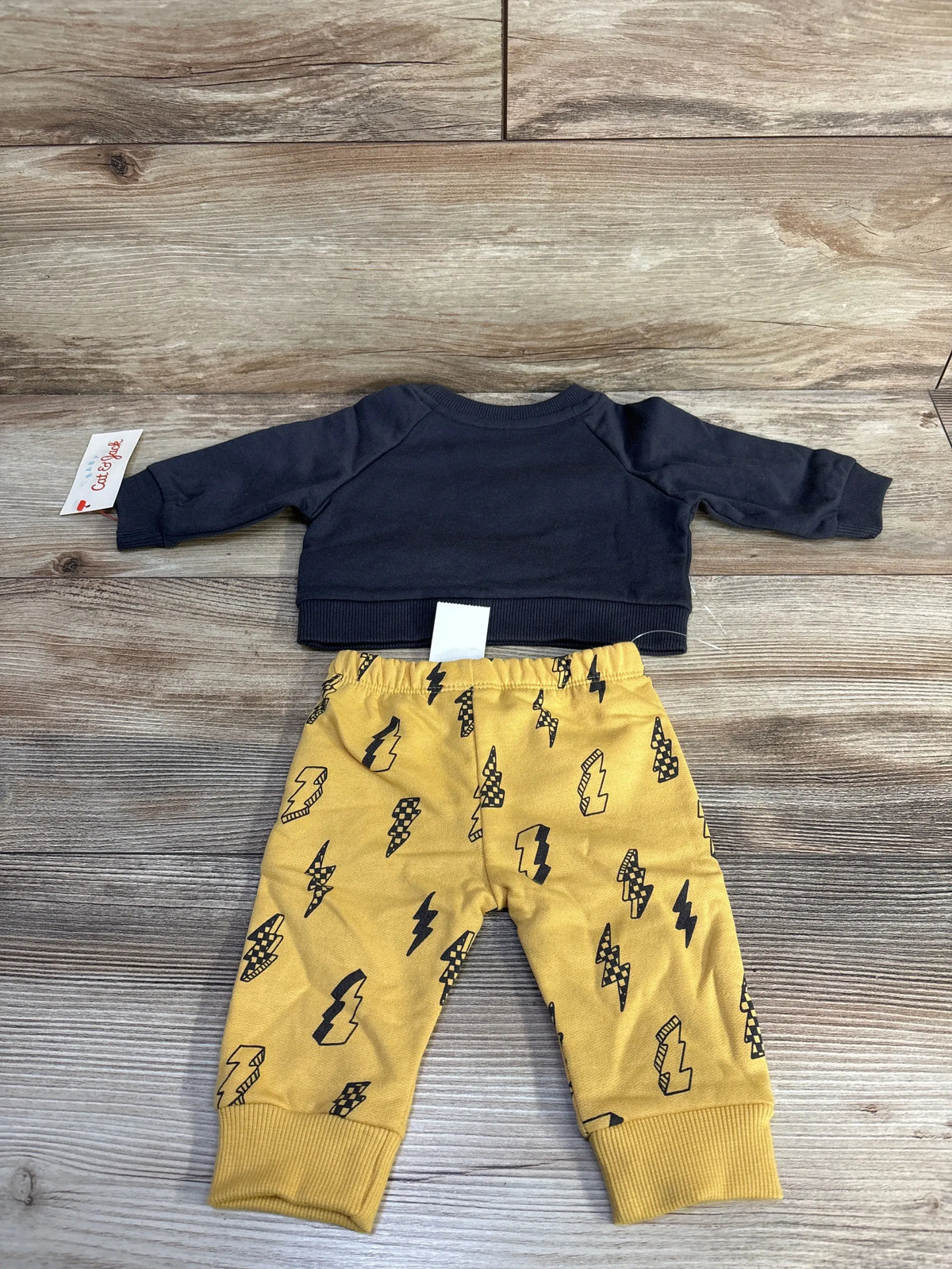 Front view of Cat and Jack 2pc Lightning Set with dark gray sweatshirt and mustard-yellow lightning-print joggers on wood grain