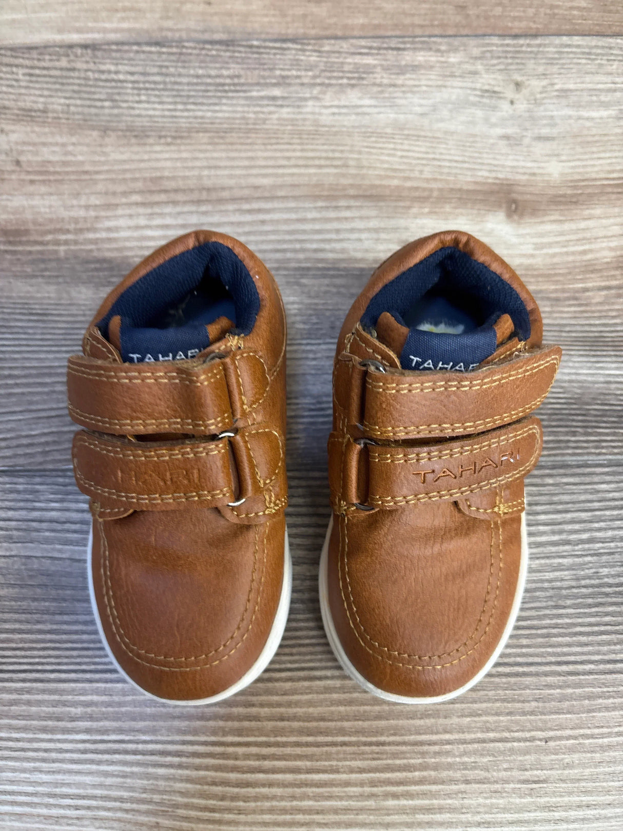 Tan Tahari baby shoes with velcro straps, navy lining, white soles on wood floor