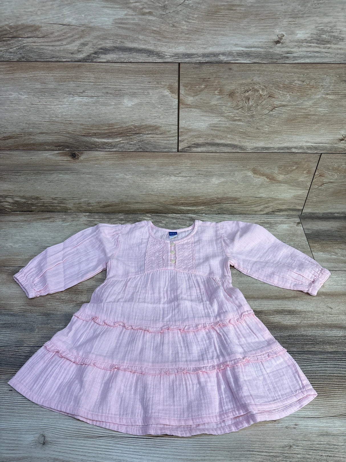 Flat lay of pink Old Navy long-sleeve tiered dress showing ruffled tiers, front buttons, textured fabric on wood background