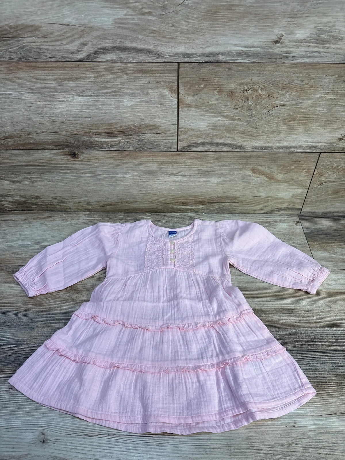 Flat lay of pink Old Navy long-sleeve tiered dress showing ruffled tiers, front buttons, textured fabric on wood background