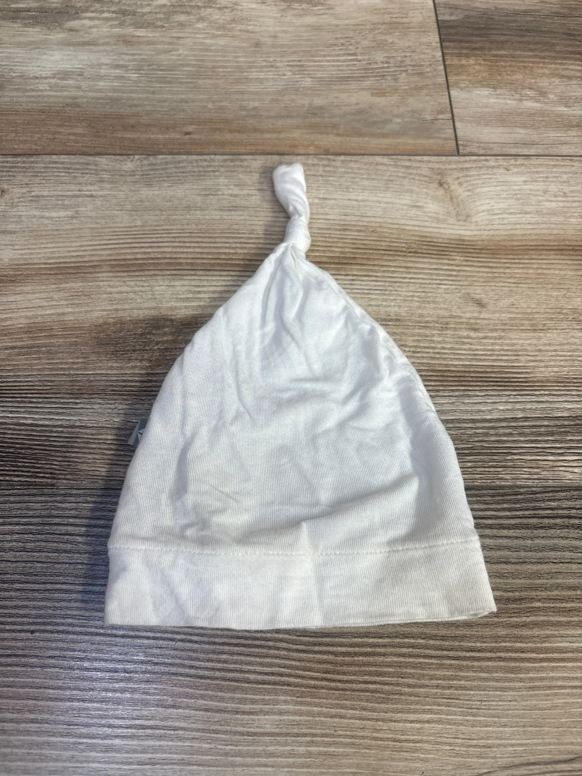 Front view of Kyte Baby white knotted cap showcasing adjustable top knot and folded band on a wood-grain surface