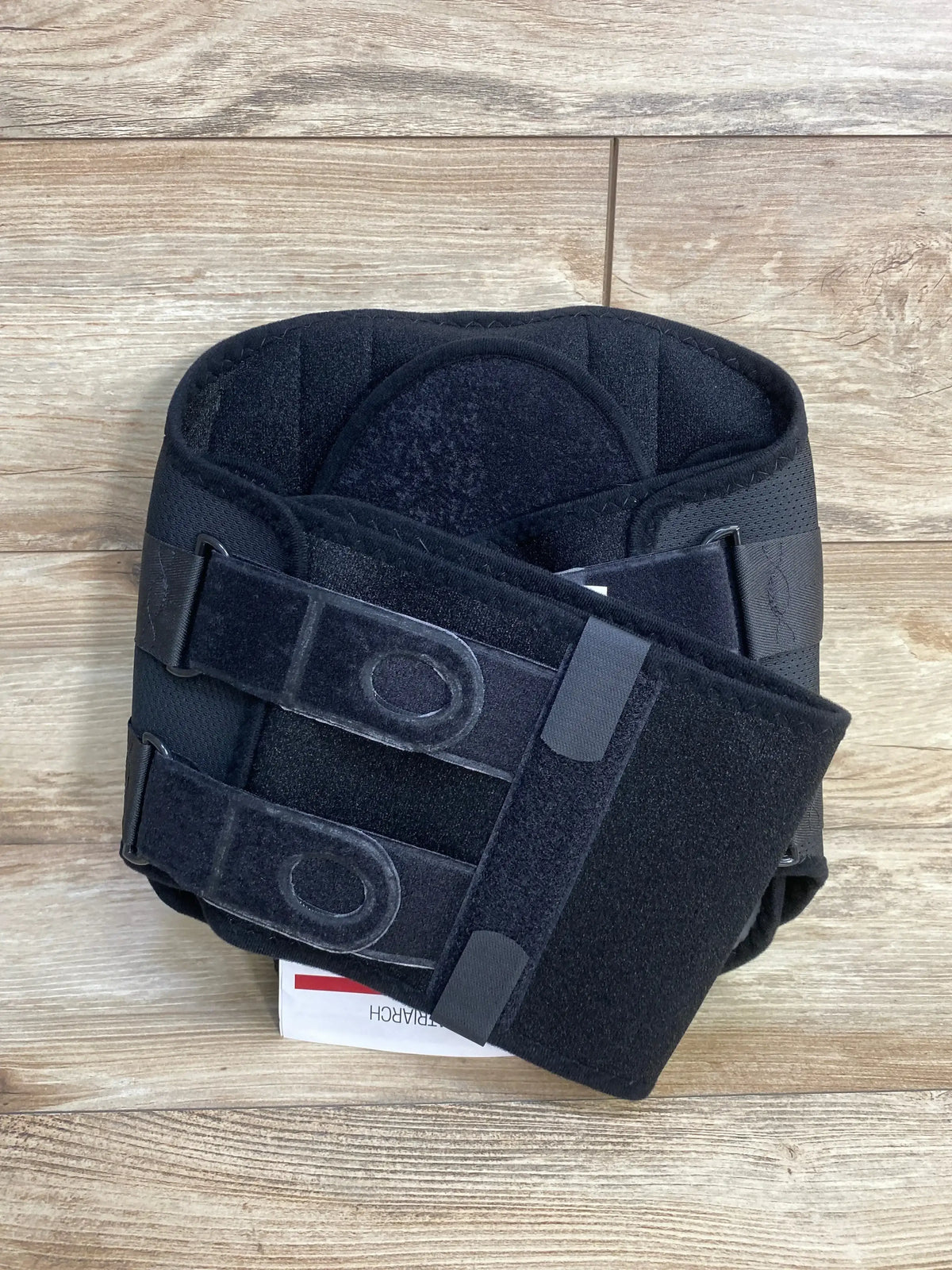 Top view of black lower back support belt with dual adjustable Velcro straps and lumbar pad on wood floor