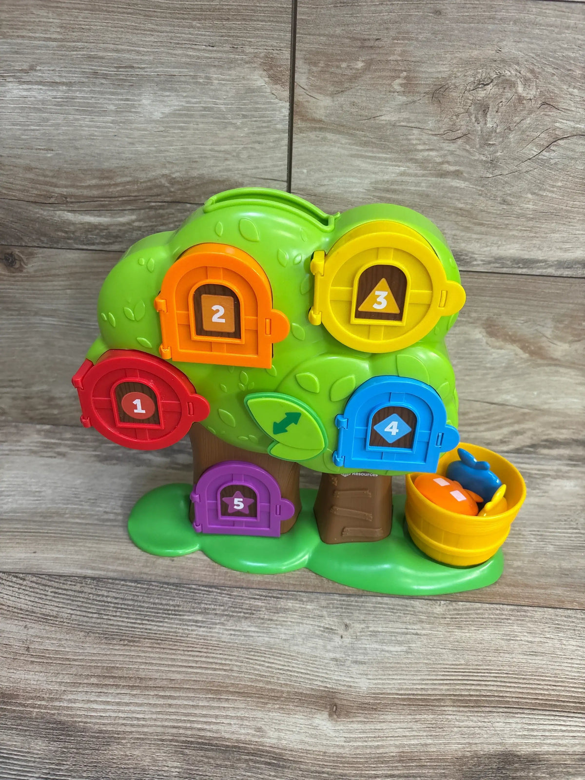 Front view of Learning Resources Hide & Seek Learning Treehouse with five colorful numbered doors and apples in a bucket