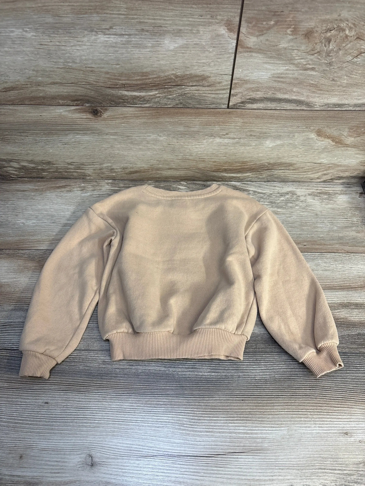 Beige kids crewneck sweatshirt with ribbed cuffs and hem on wood background