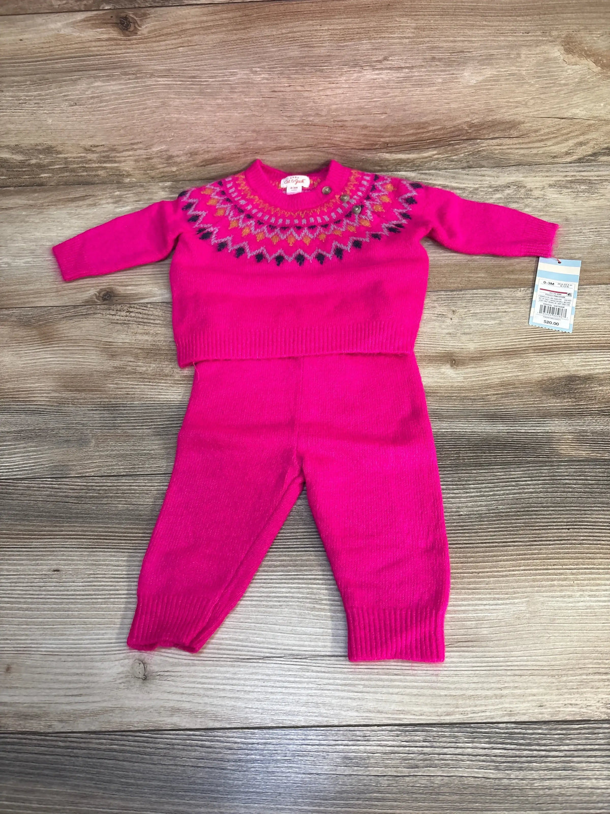 Flat lay of Cat & Jack newborn 0-3M hot pink Fair Isle knit sweater and matching pants showcasing multicolor yoke and original price tag on wood background