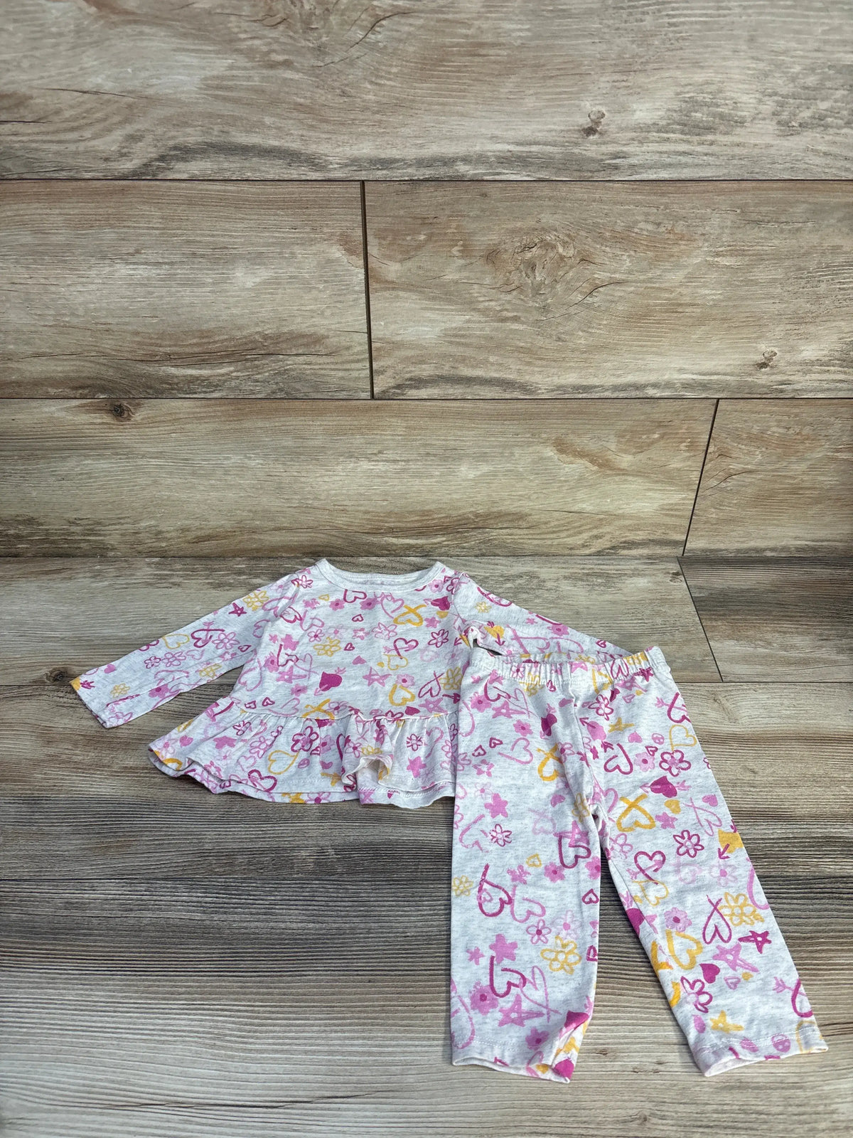 Front view of First Impressions peplum top and bottoms set showcasing ruffle detail and heart and flower print on wood flooring