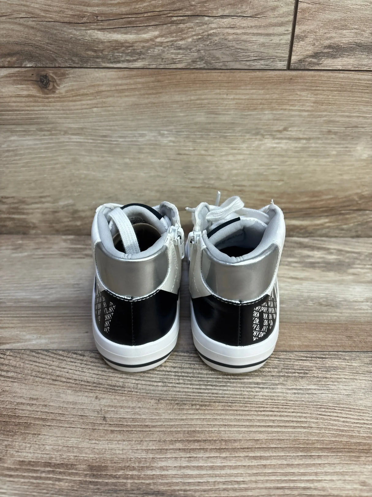 Rear view of DKNY Hannah Leena girls' white high-top sneaker showing back zipper, silver heel and DKNY logo on wood floor