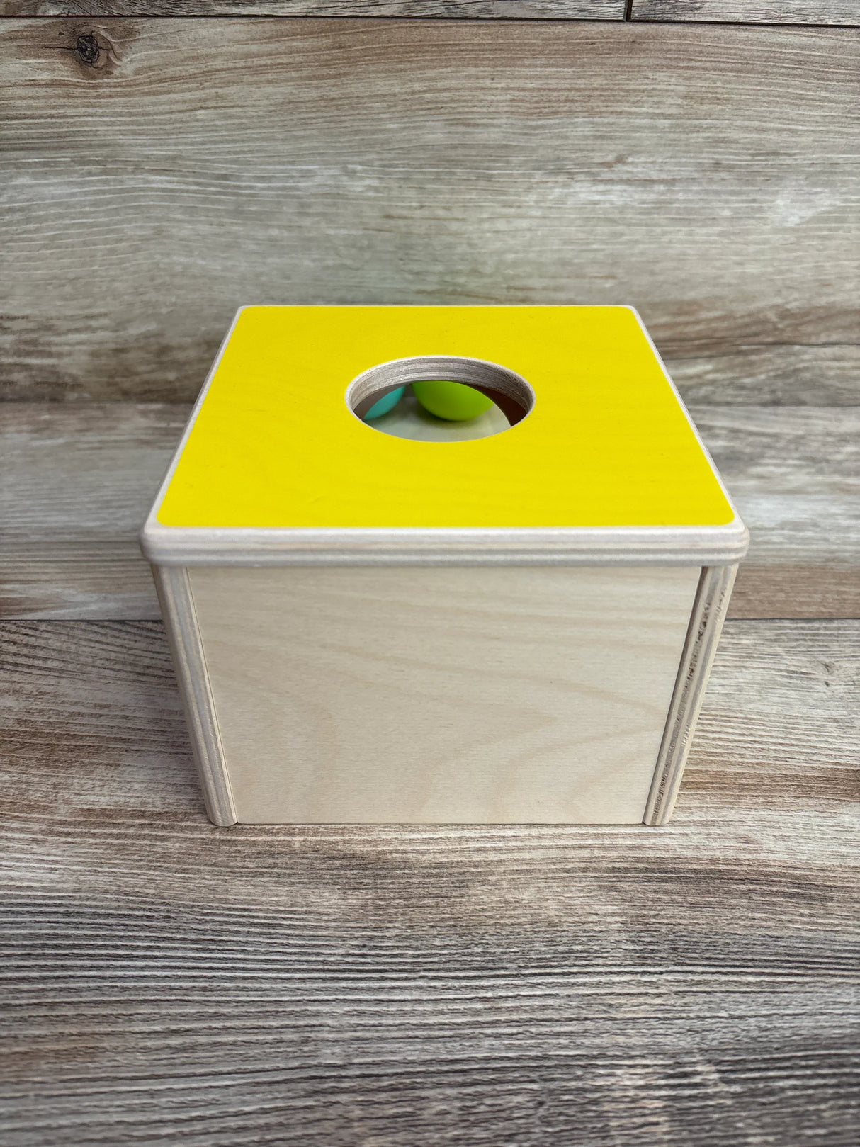 Wooden Montessori toy box with yellow top panel and circular hole, on wooden surface