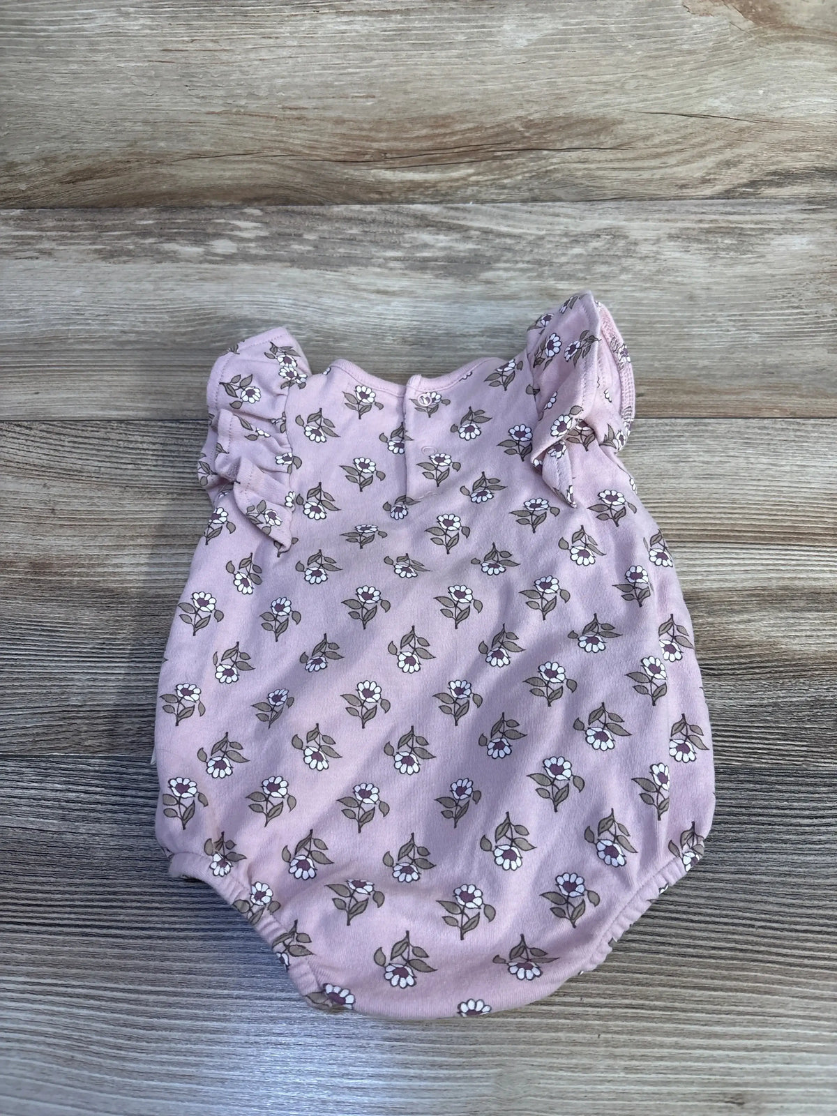 Flat lay of pink Rabbit and Bear organic floral bubble romper with ruffle sleeves and elastic leg openings on wood background