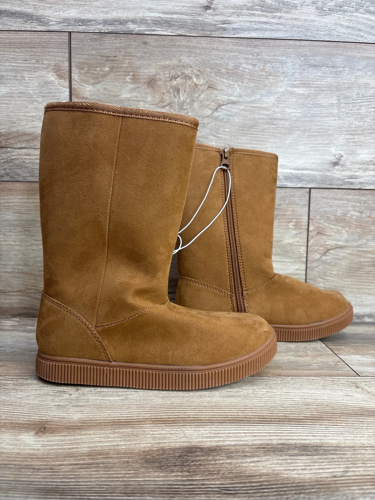 Brown suede children's boots with side zipper and flat rubber sole on wood background