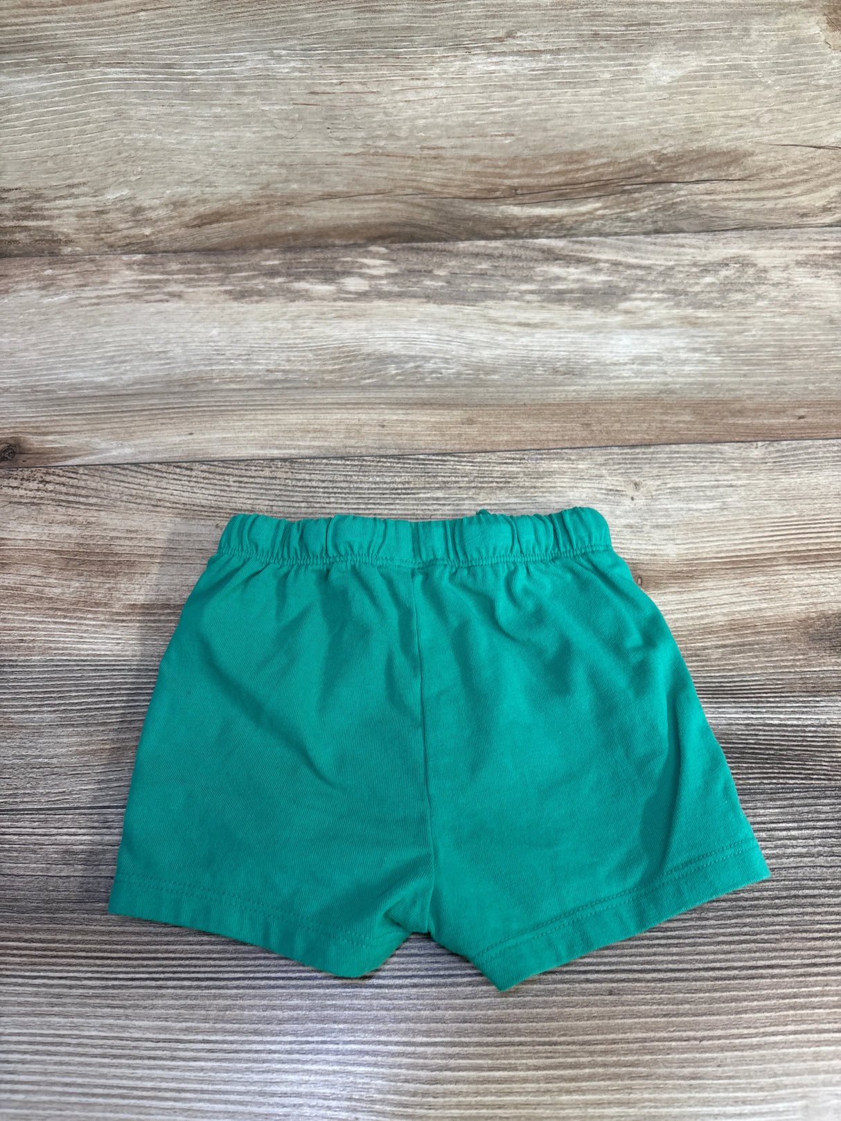 Flat lay of Cat & Jack green toddler shorts showing elastic waistband and short hem on light wood background