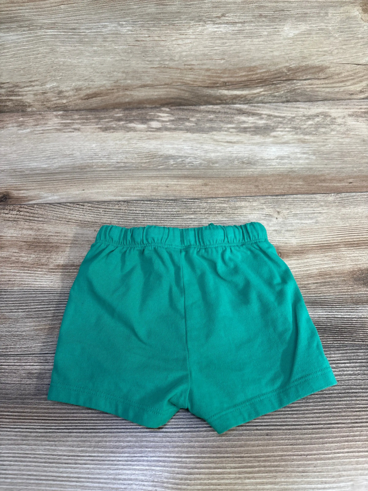 Flat lay of green Cat & Jack drawstring shorts in size 12 months showing elastic waistband on a wood-grain background