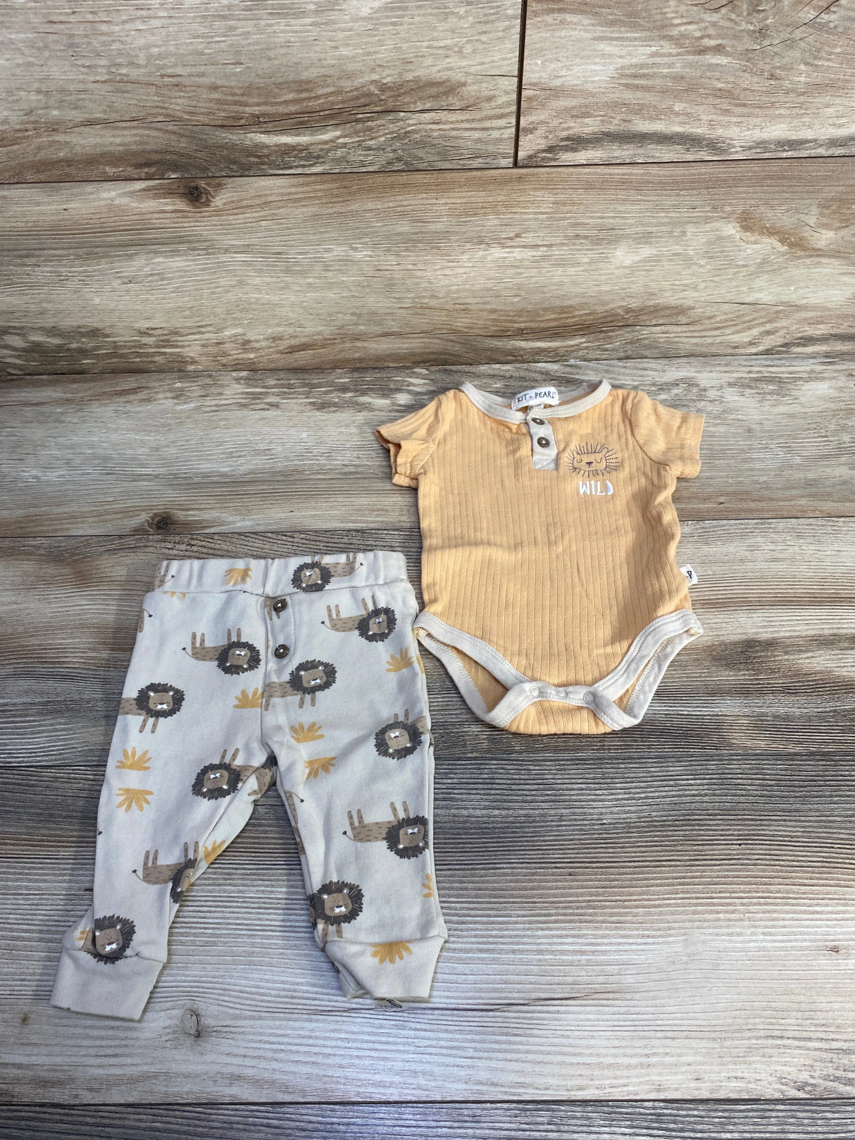 Baby outfit set with yellow wild print bodysuit and lion print pants on wood floor