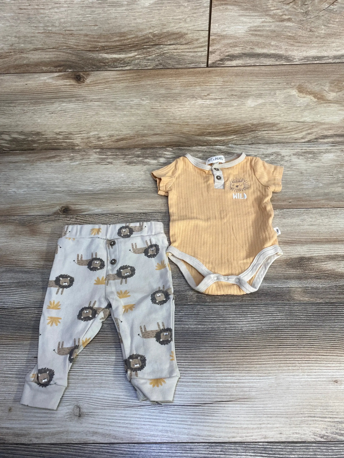 Baby outfit set with yellow wild print bodysuit and lion print pants on wood floor