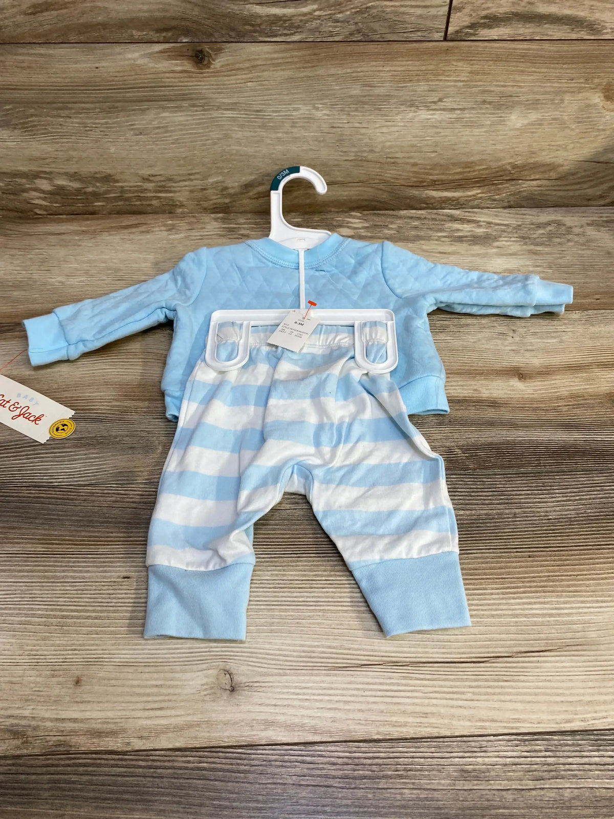 Front view of Cat and Jack blue newborn two piece outfit on hanger with quilted top and striped pants on wood background