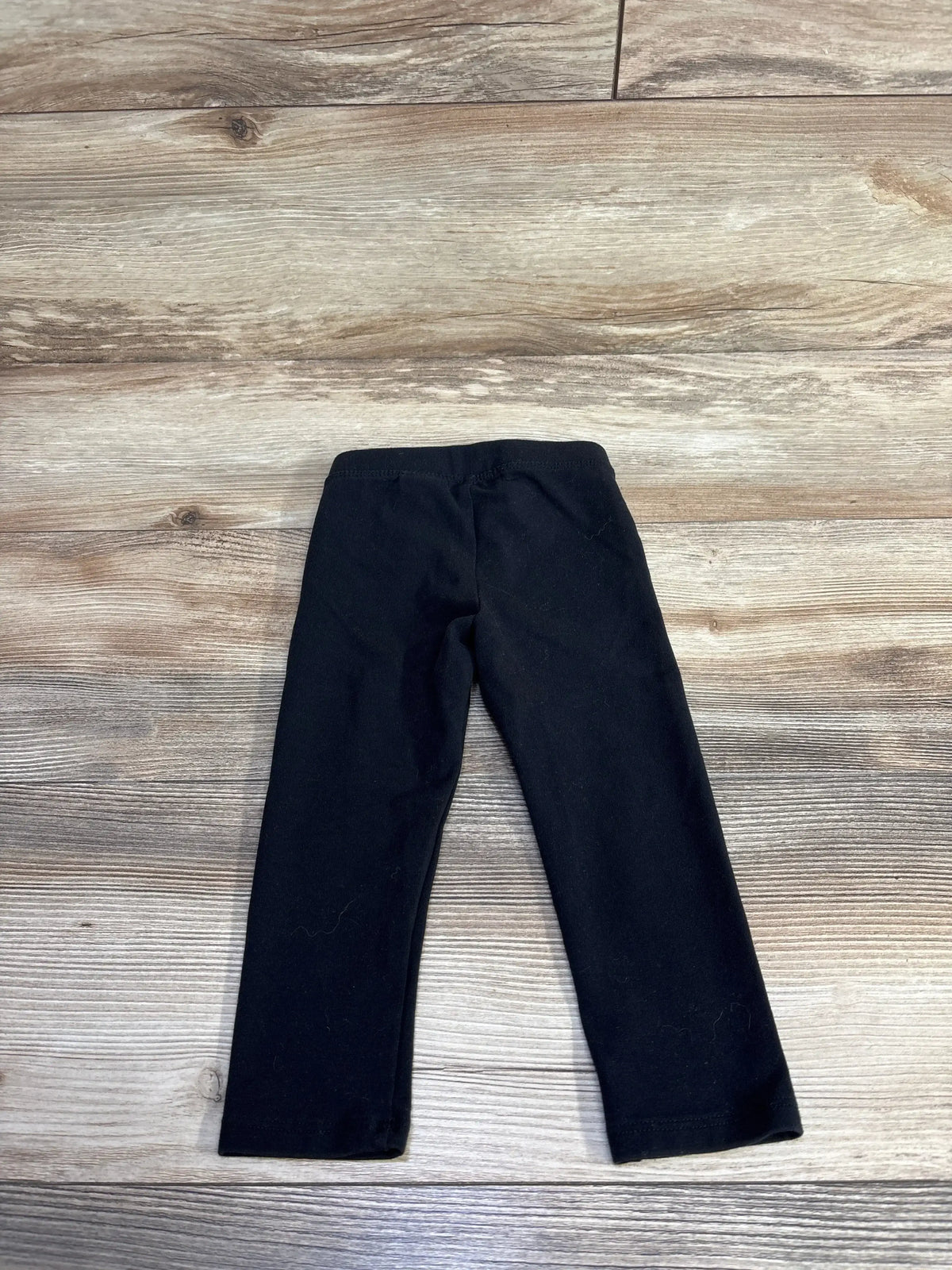 Flat lay of Amazon Essentials toddler black leggings showcasing elastic waistband and straight legs on wood background