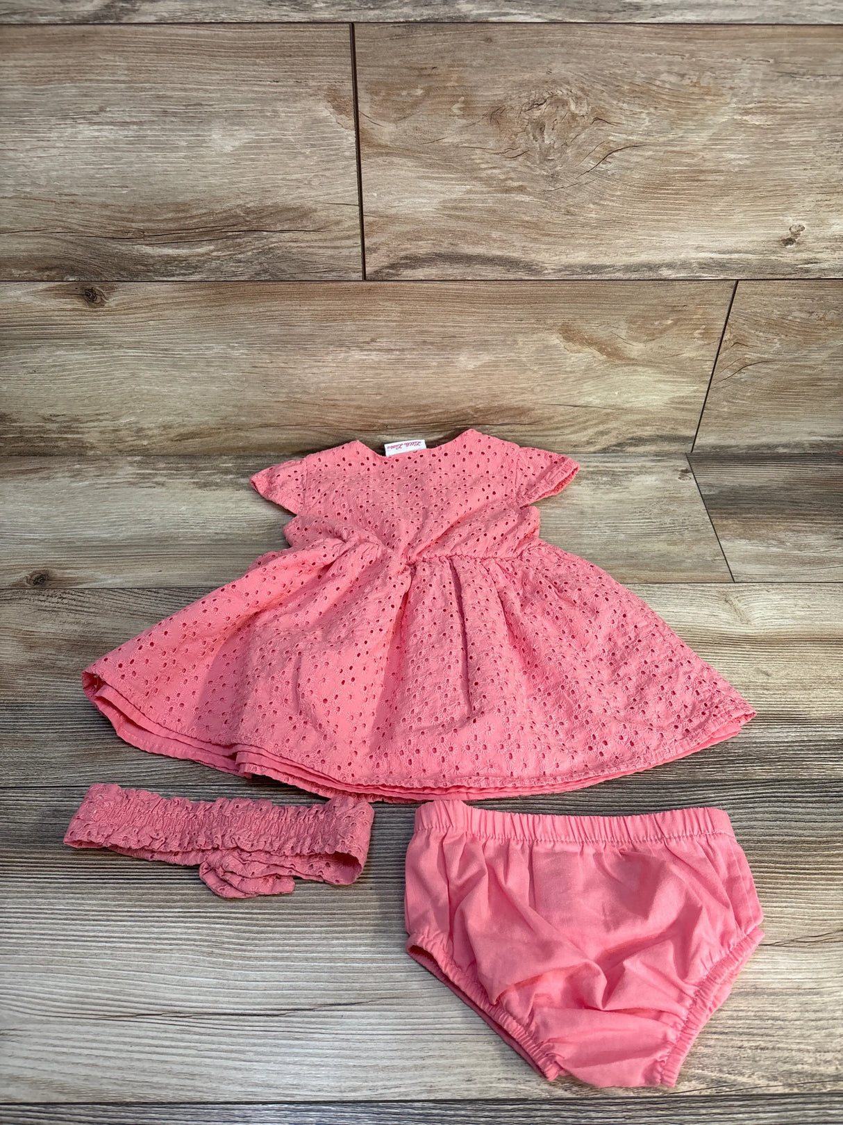 Pink eyelet baby dress set with matching headband and bloomers on wood background