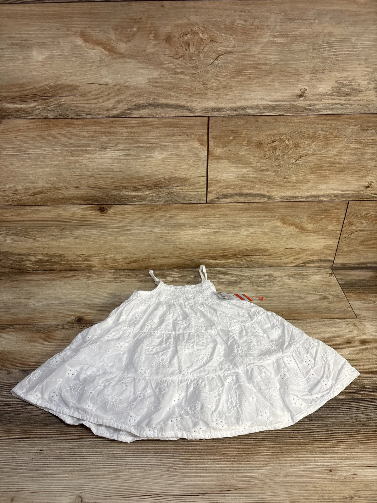 Front view of Cat & Jack white eyelet embroidered dress showcasing sleeveless tiered design and smocked upper on wood flooring