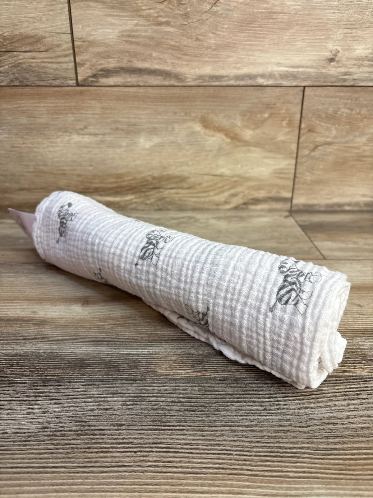 Rolled view of Amazing Baby muslin swaddle blanket in zebra print white showcasing textured fabric on a wood-look floor