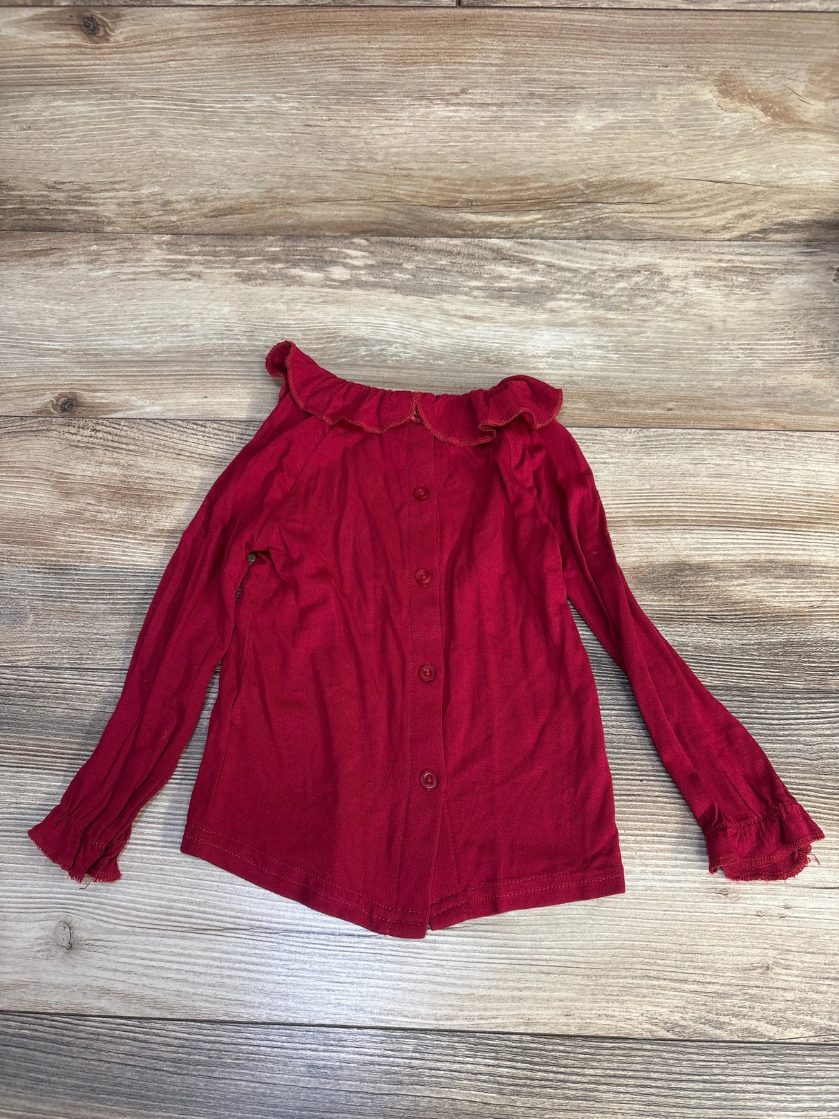 Red long sleeve toddler shirt with ruffled collar and sleeves on wood background
