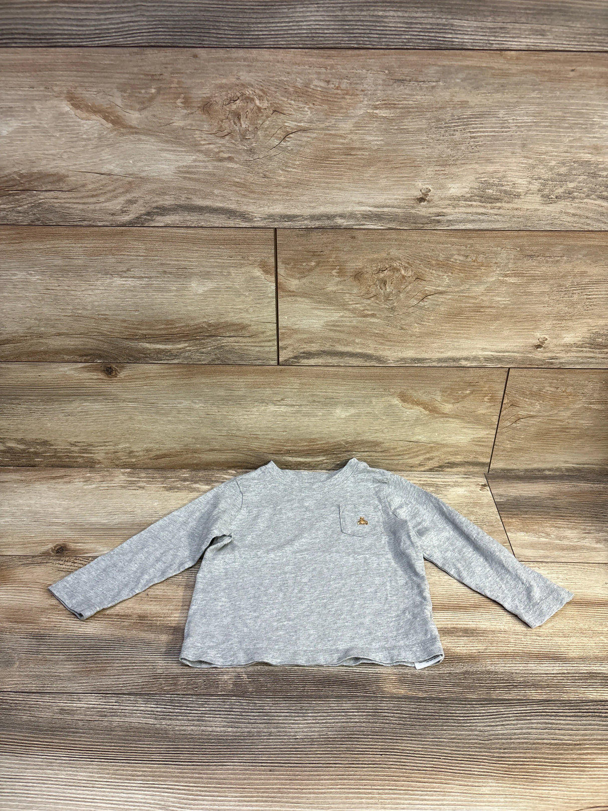 Front view of gray Baby Gap long-sleeve toddler pocket shirt size 18 to 24 months showcasing small embroidered animal on chest pocket with wood-plank background