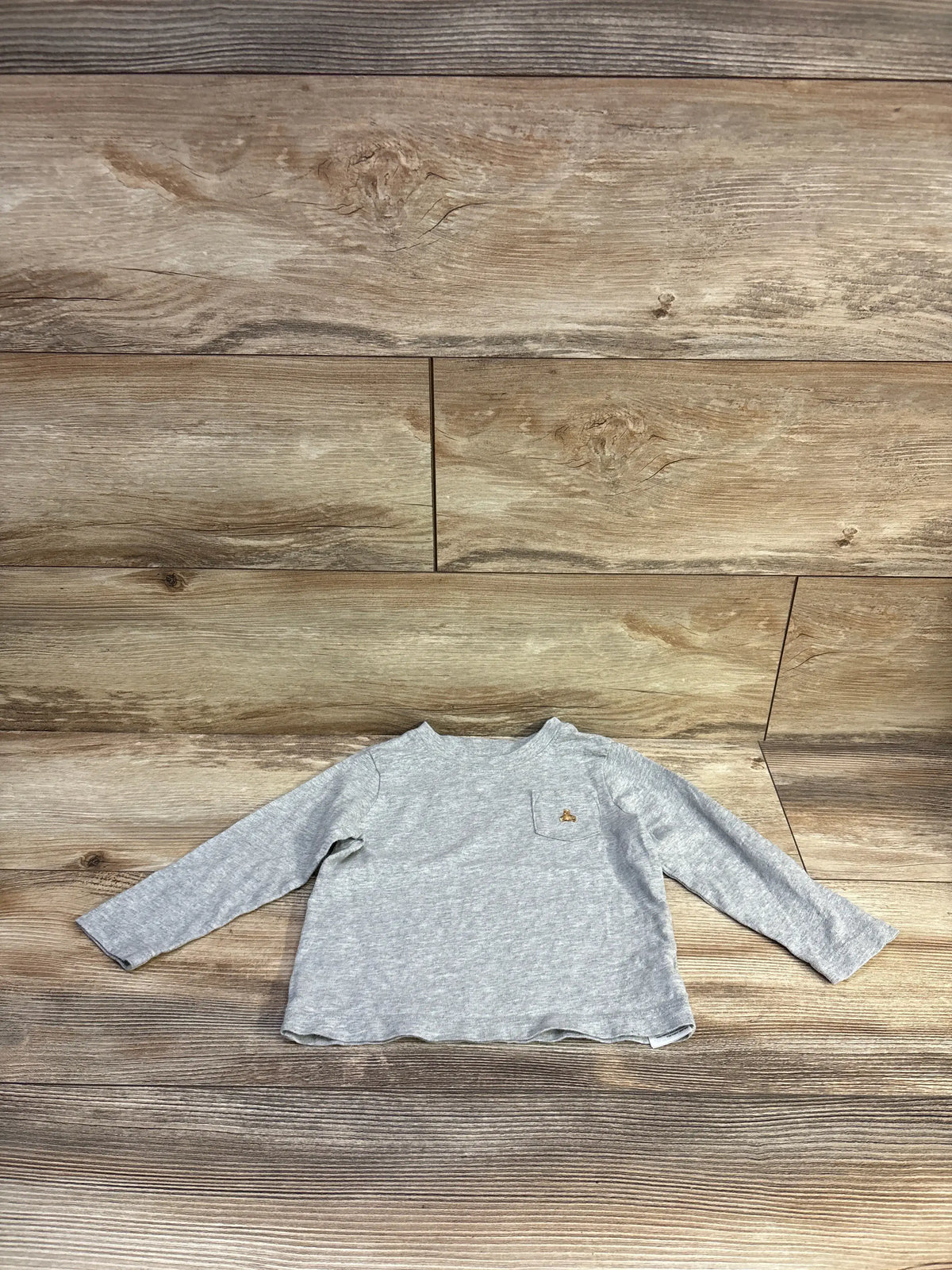 Front view of gray Baby Gap long-sleeve toddler pocket shirt size 18 to 24 months showcasing small embroidered animal on chest pocket with wood-plank background