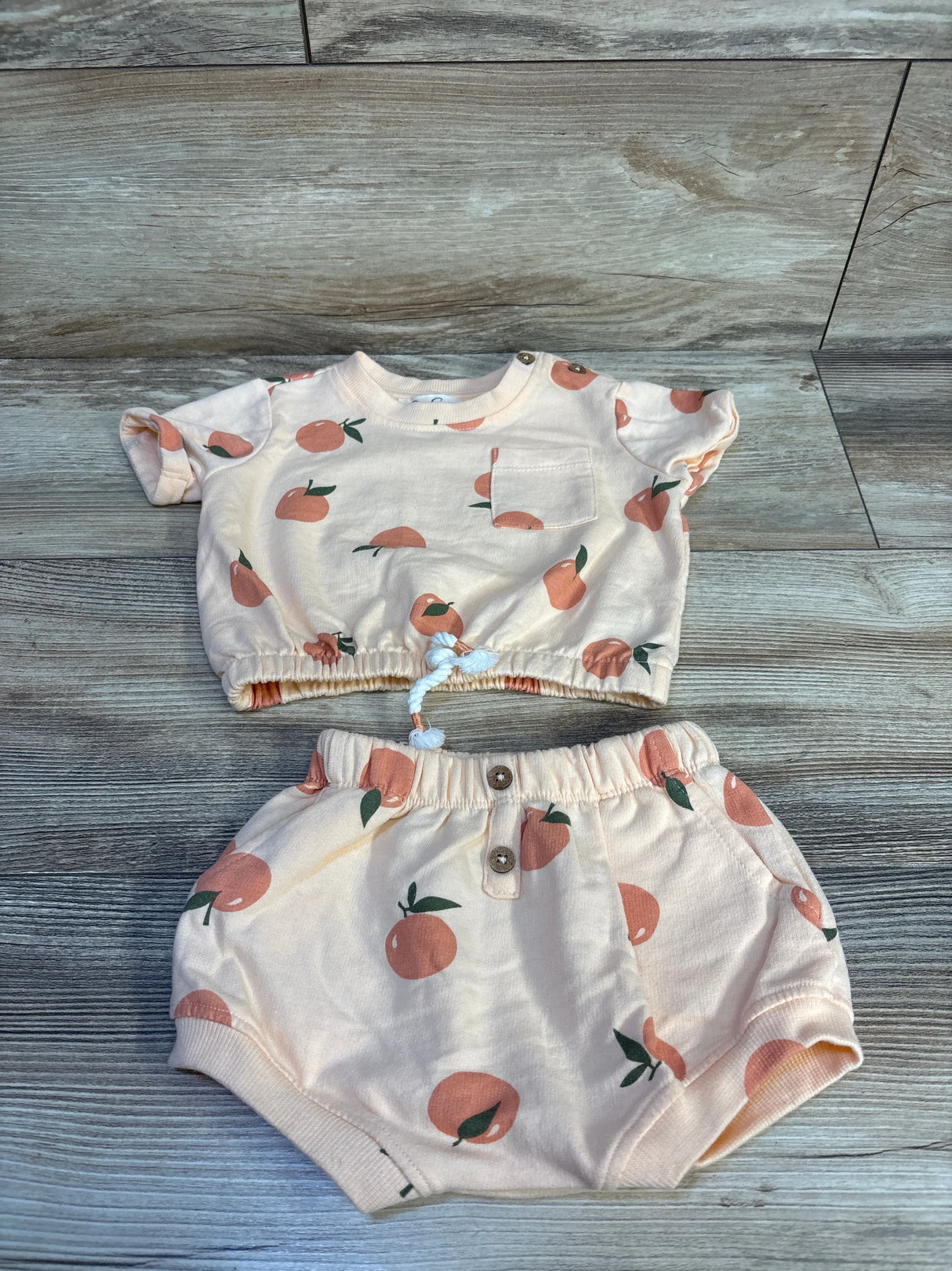 Flat lay of peach-print 2-piece baby shirt and shorts set 3-6m with drawstring crop top and elastic-waist bloomers