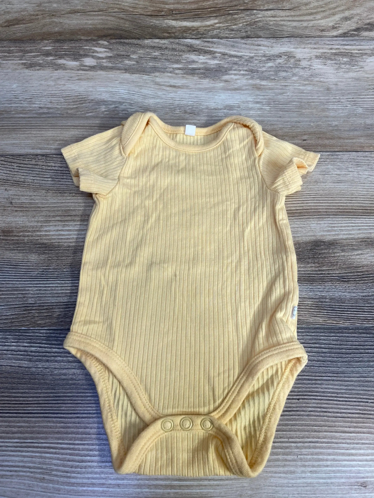 Top-down view of Mori yellow ribbed newborn bodysuit (0-3M) showcasing ribbed texture and three-snap crotch on wood background