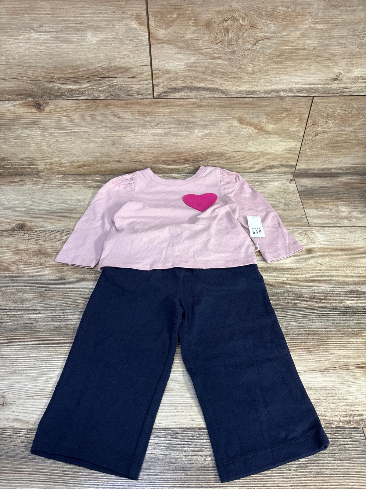 Front view of Baby Gap two-piece set showcasing pink puff sleeve shirt with heart applique and navy pants on a wood floor