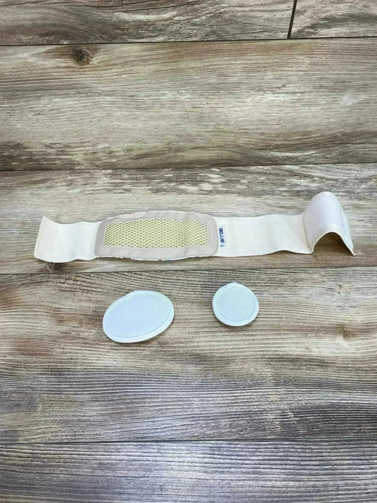 Top-down view of Bojje umbilical hernia belt showing mesh pressure pad and two detachable oval support pads on wood background