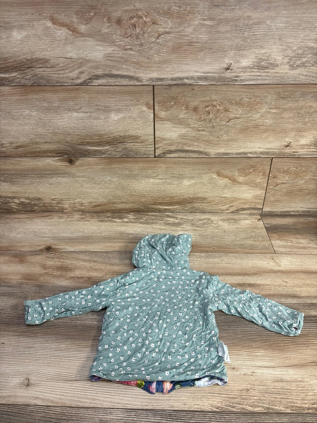 Back view of Posh P reversible baby hoodie in blue with white daisies, showing hood and quilted back on wood background