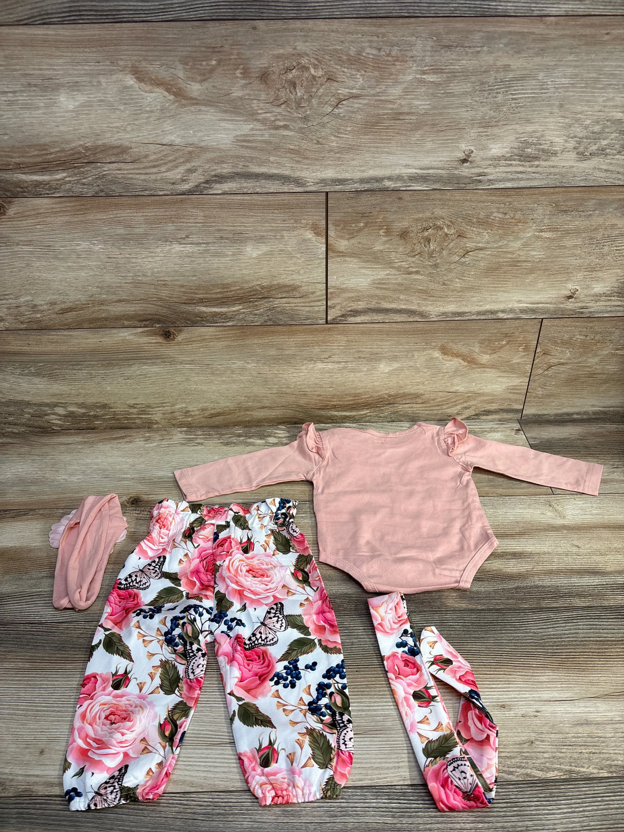 Baby girl outfit set with pink long-sleeve bodysuit, floral pants, headband on wood floor