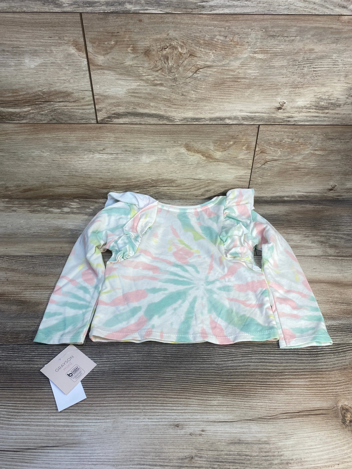 Pastel tie-dye long sleeve toddler shirt with ruffle shoulders on wood background