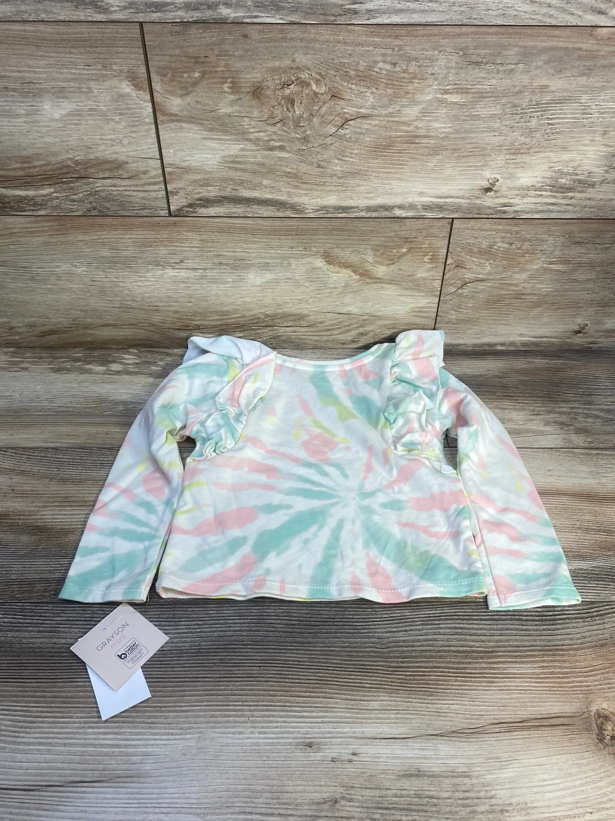 Pastel tie-dye long sleeve toddler shirt with ruffle shoulders on wood background