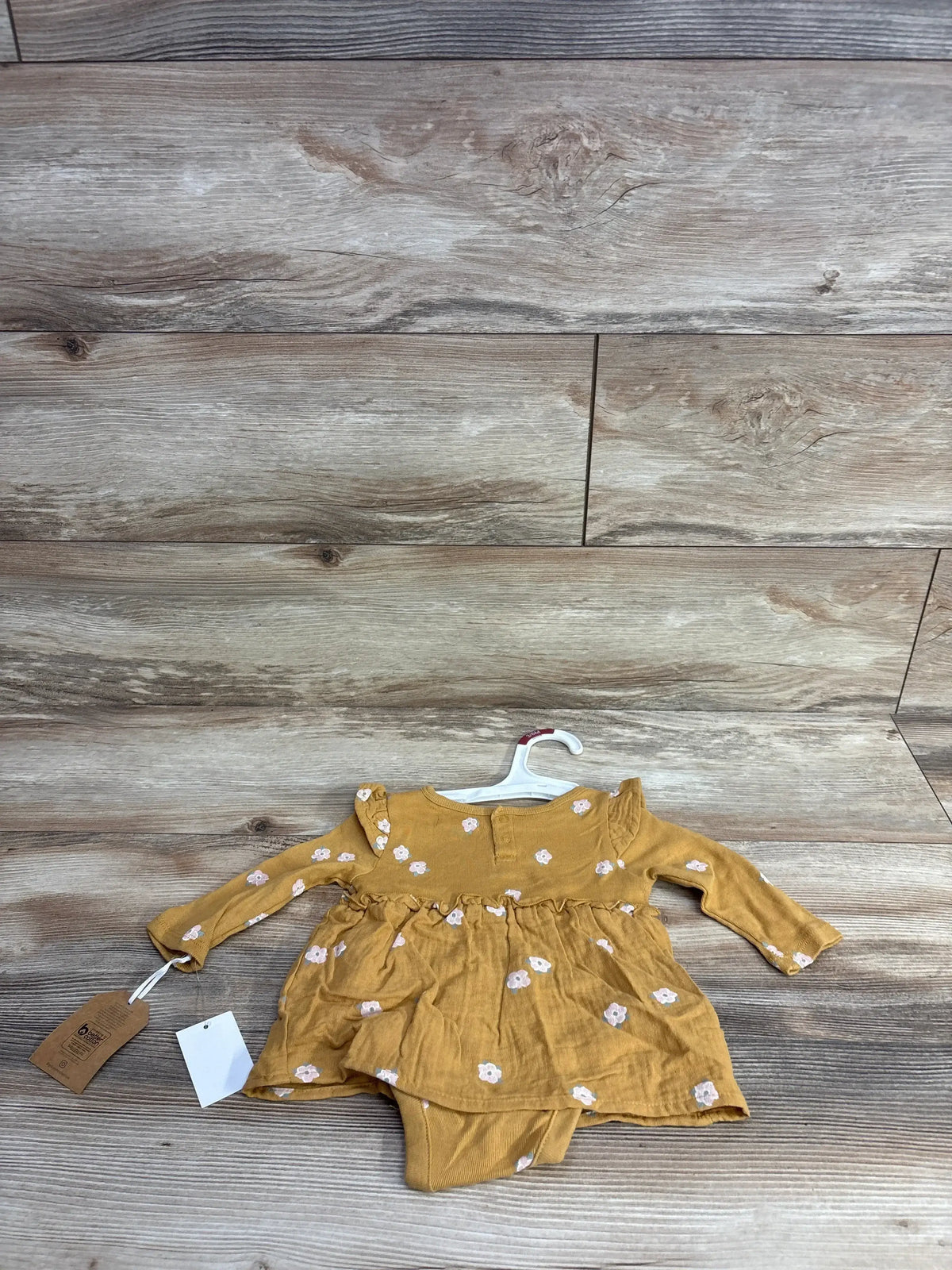 Mustard yellow baby dress with floral pattern and ruffle details, long sleeves, on hanger