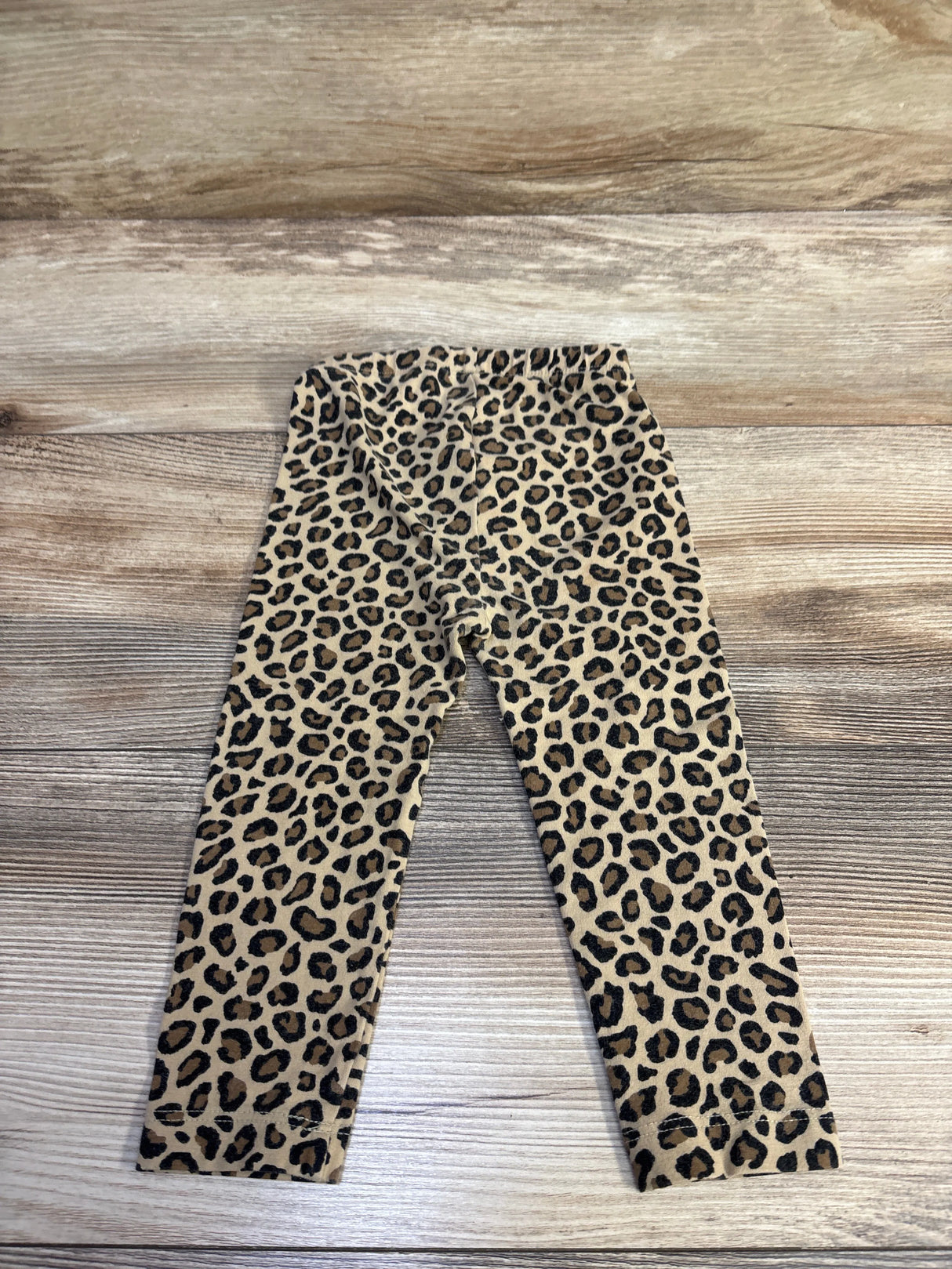 Flat lay of Old Navy toddler leggings size 18-24 months showing tan leopard print and elastic waist on wood background