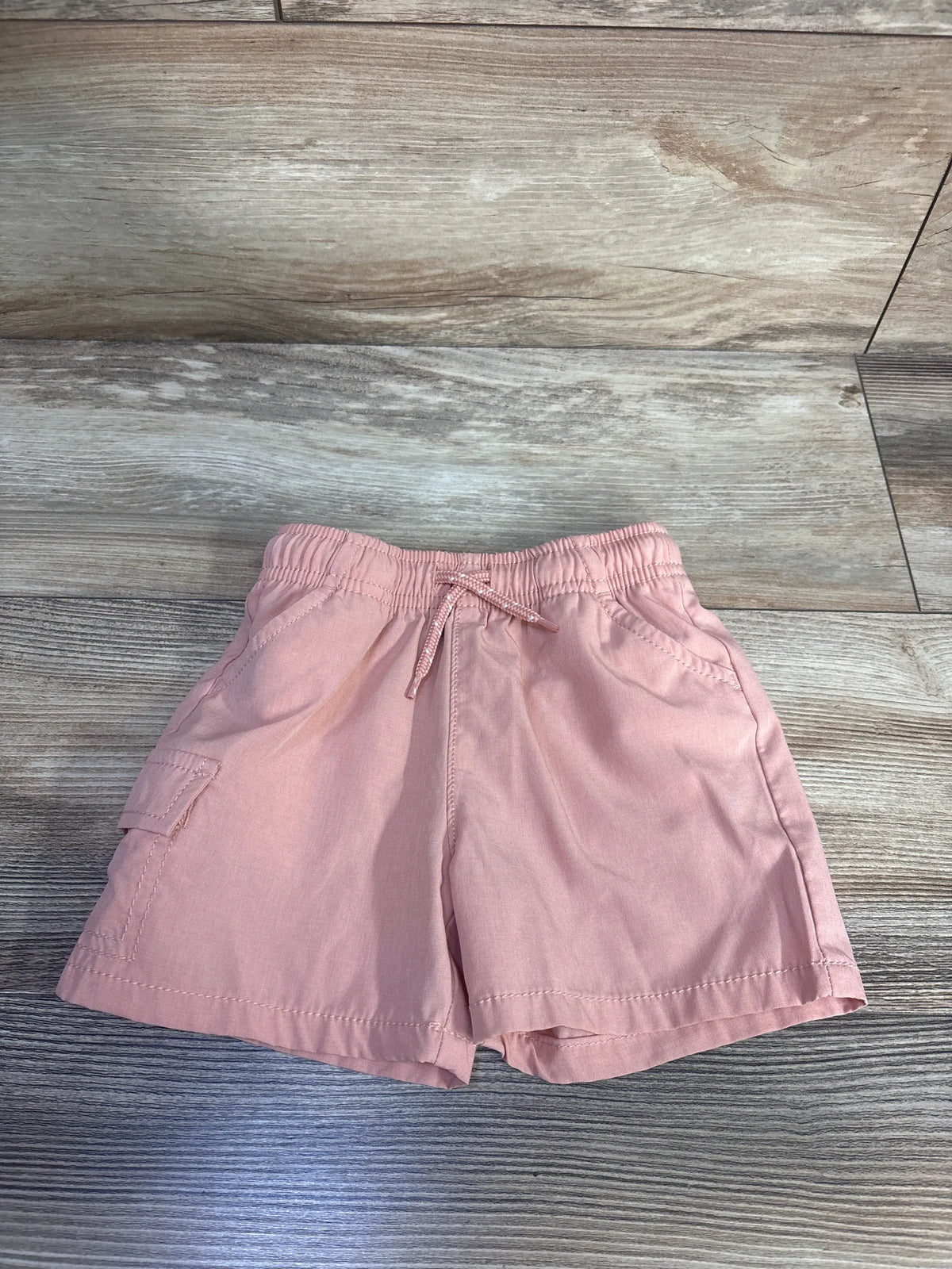 Front view of Oshkosh orange board shorts showcasing elastic waist, drawcord, side pockets, and lightweight fabric on a wood floor