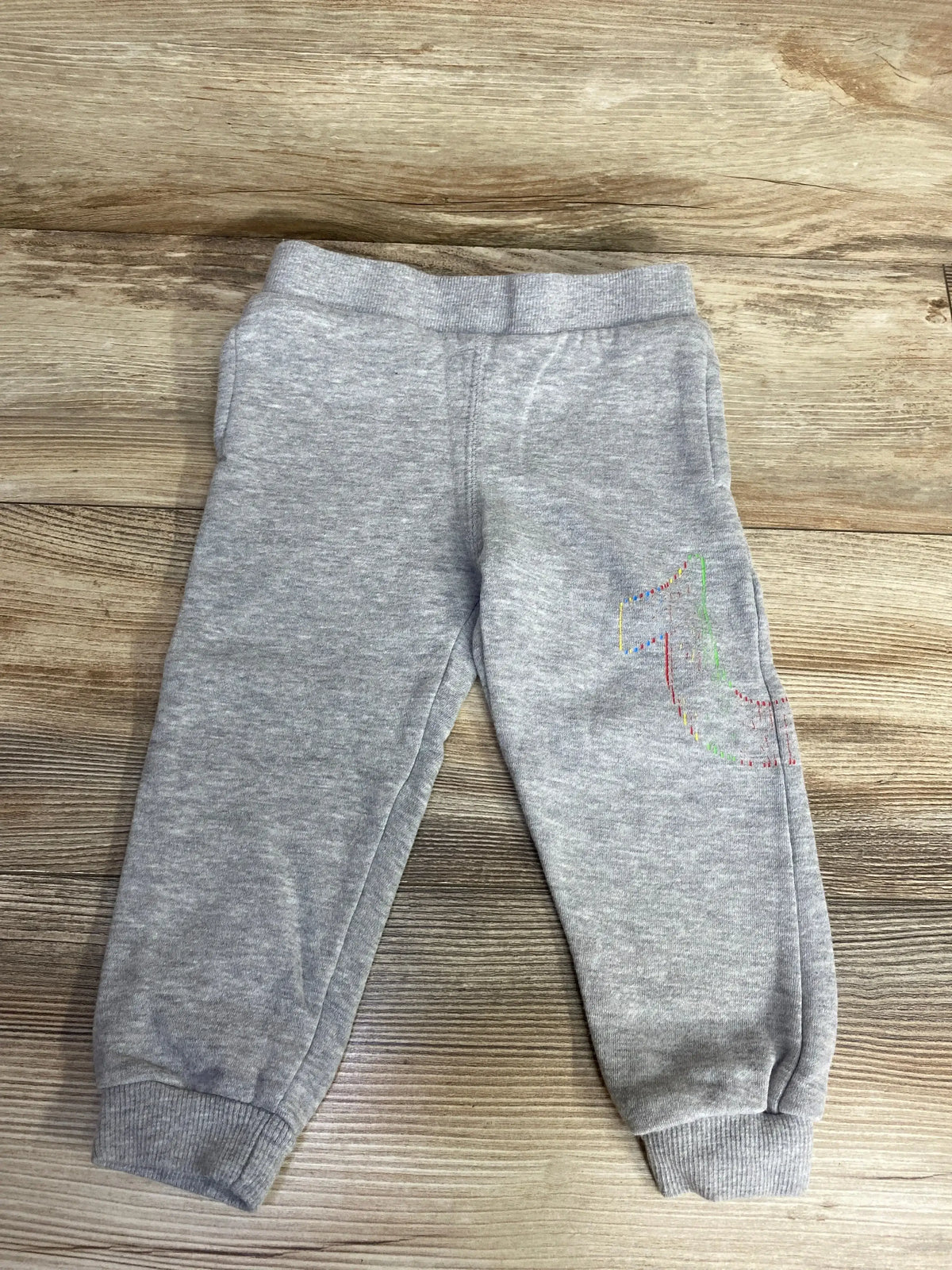Gray toddler sweatpants with multicolored stitched number one on leg, laid on wooden floor