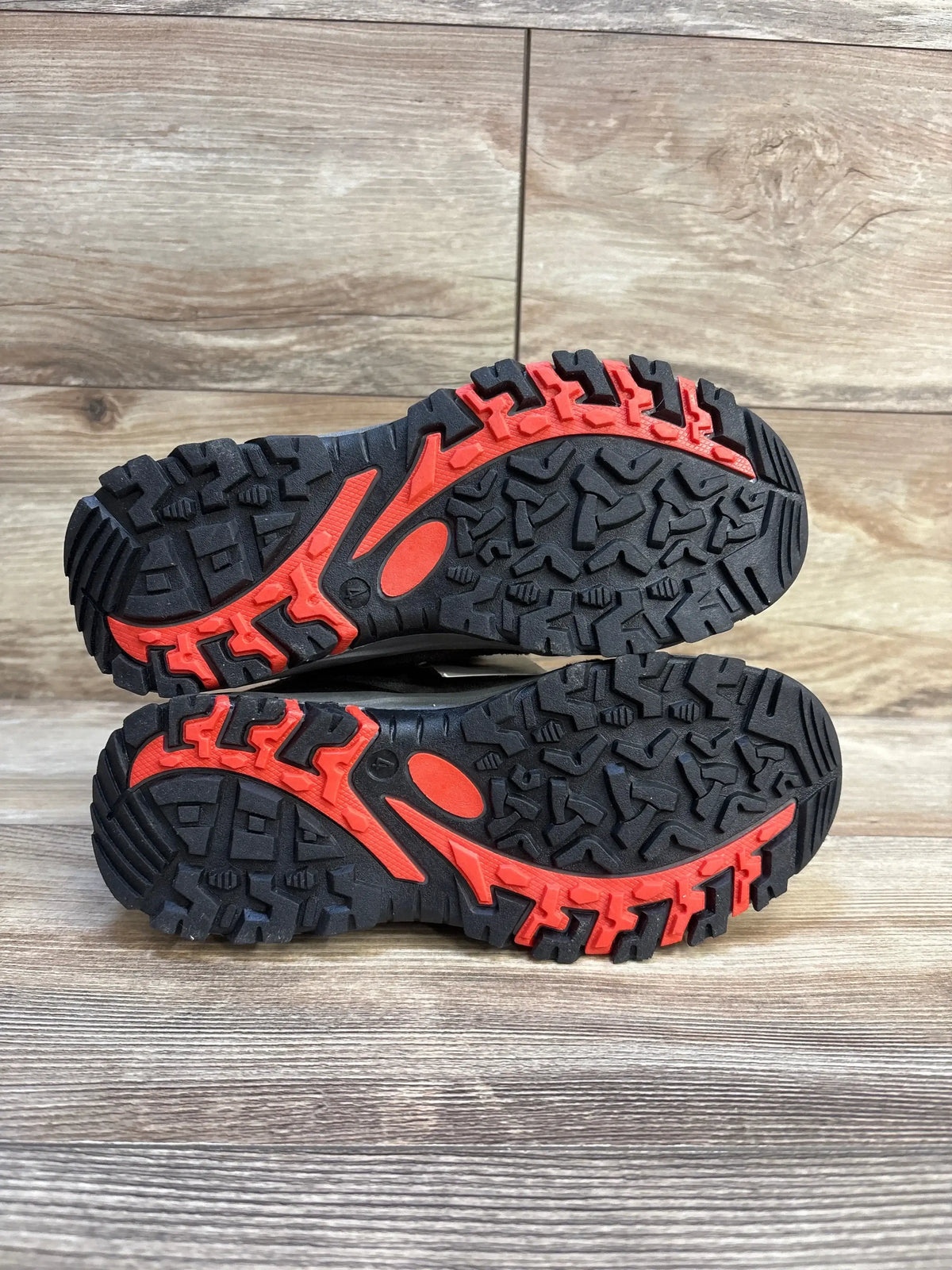 Bottom view of Cat & Jack Patsy kids’ hiking boots (size 4Y) showcasing black and red rugged soles on wood background