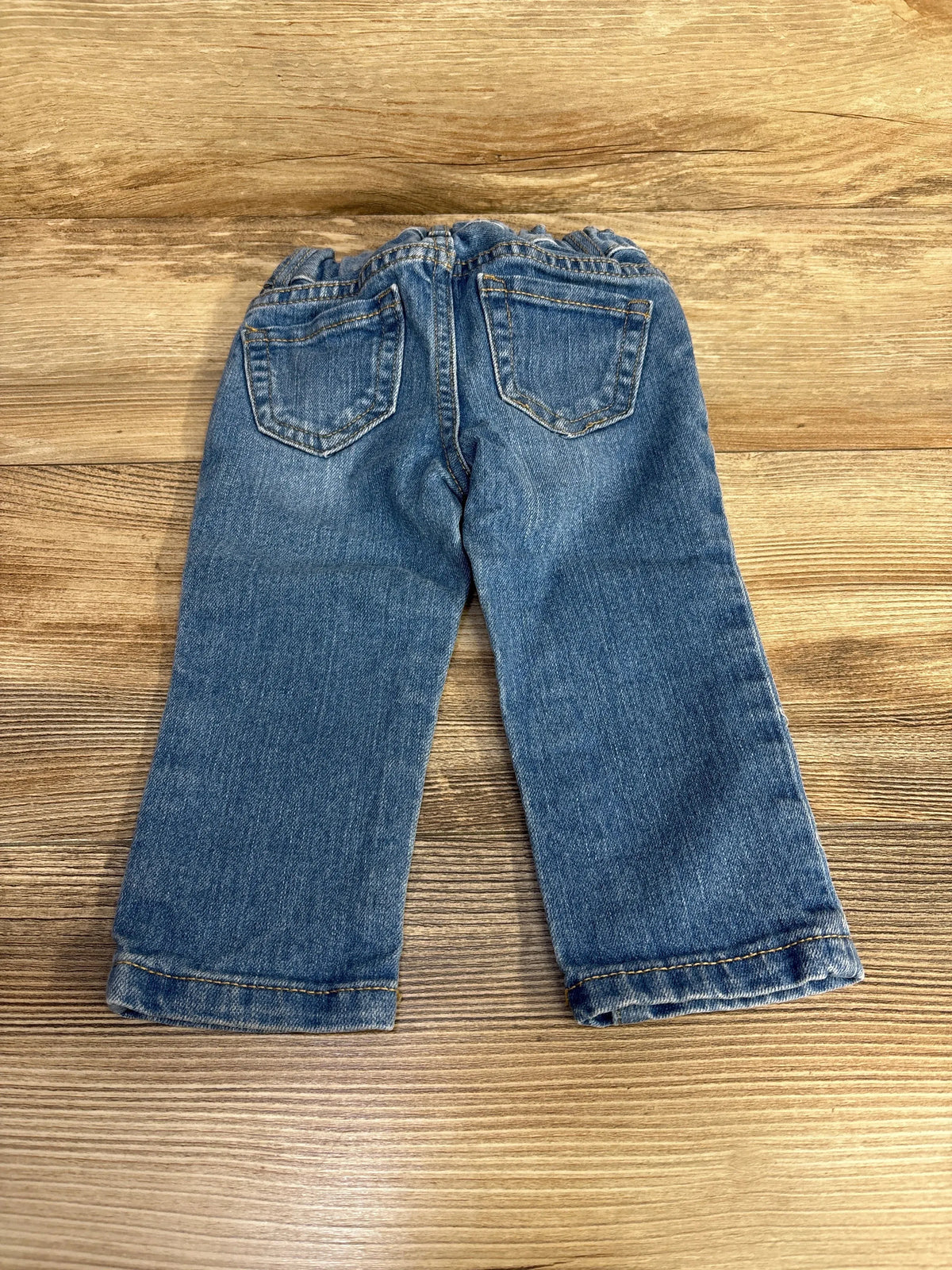 Back view of Children’s Place toddler skinny blue jeans showcasing elastic waistband and two back pockets on wood background