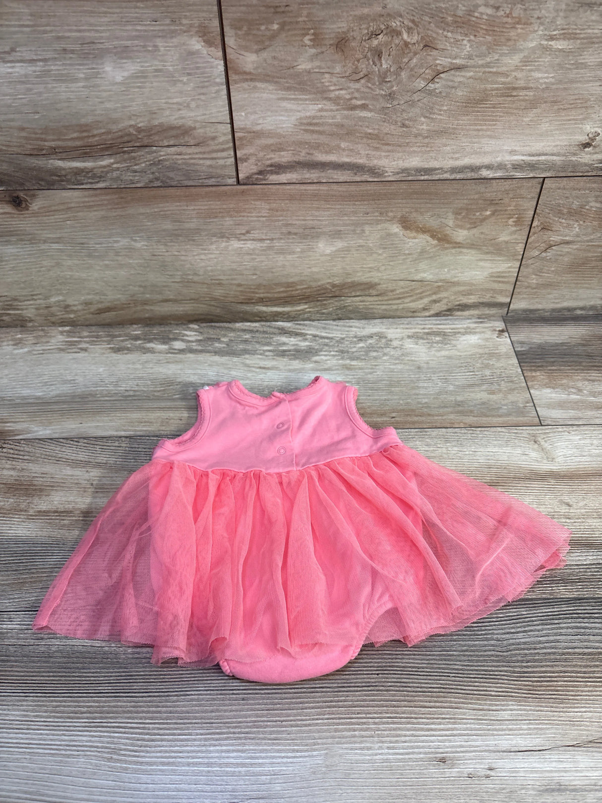 Top-down view of pink tulle baby bodysuit dress showing layered tulle skirt and snap-back bodice on wood background